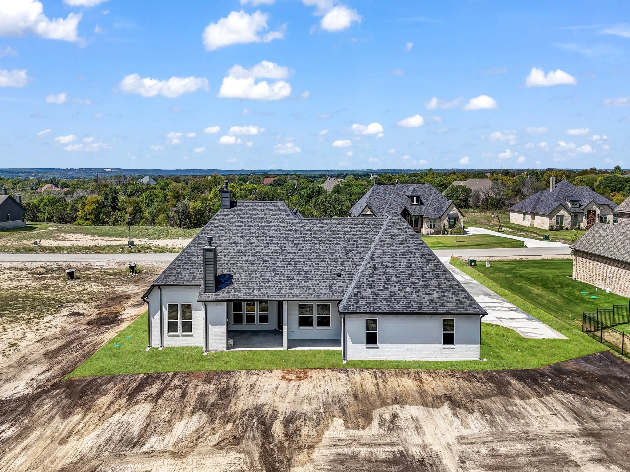A newly built white house with a dark gray roof, surrounded by green grass, under a blue sky with scattered clouds, located in a suburban neighborhood.