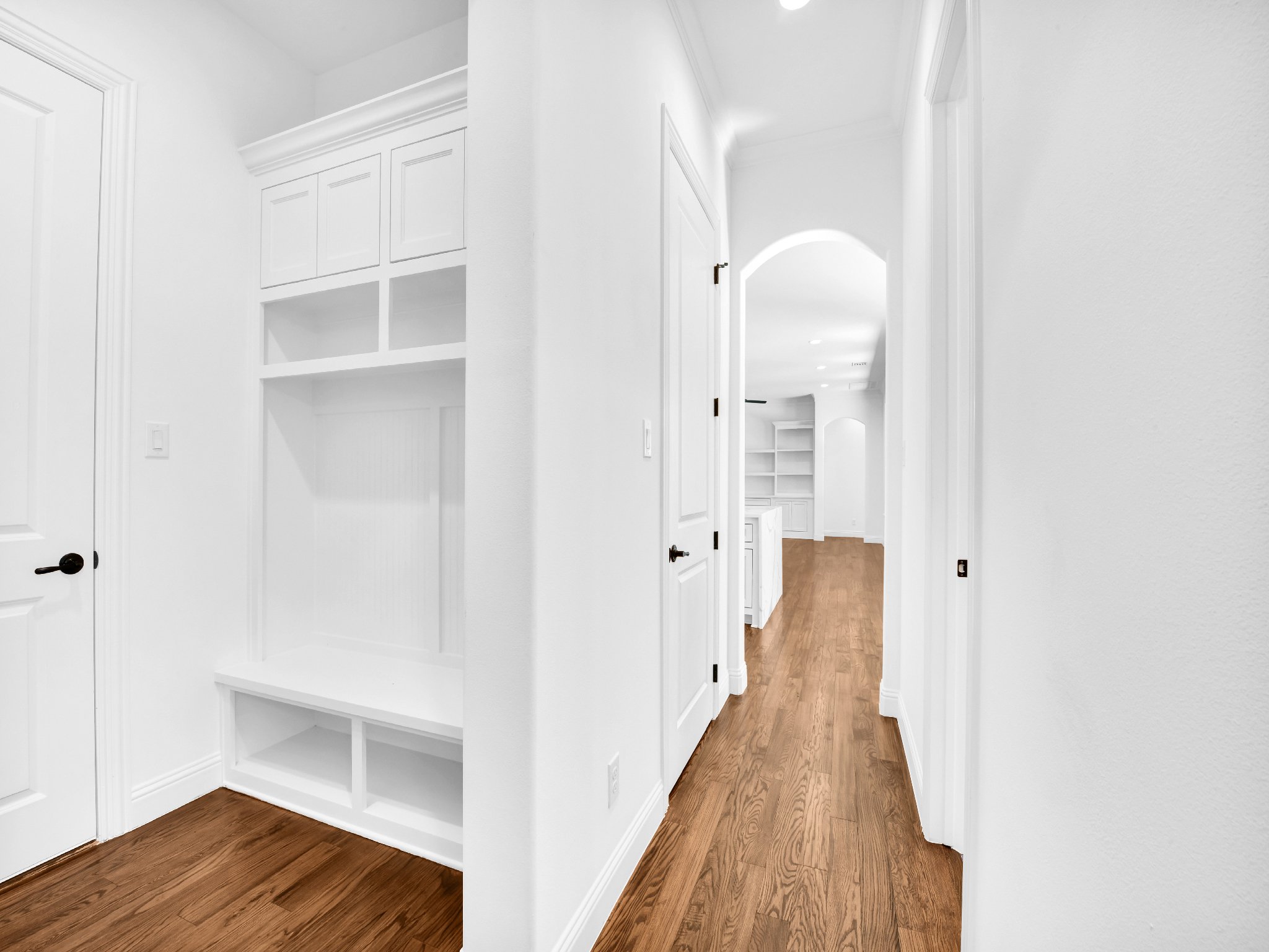 White hallway with wooden floors, built-in shelves, and doorways leading to other rooms in a house.