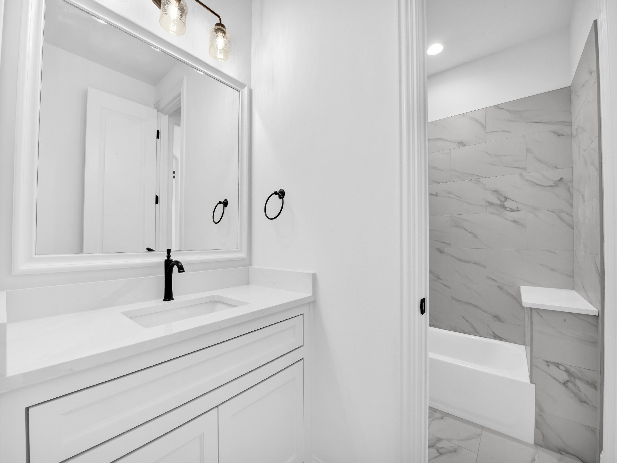 Modern bathroom with white vanity, large mirror, black faucet, and a walk-in shower with marble walls.