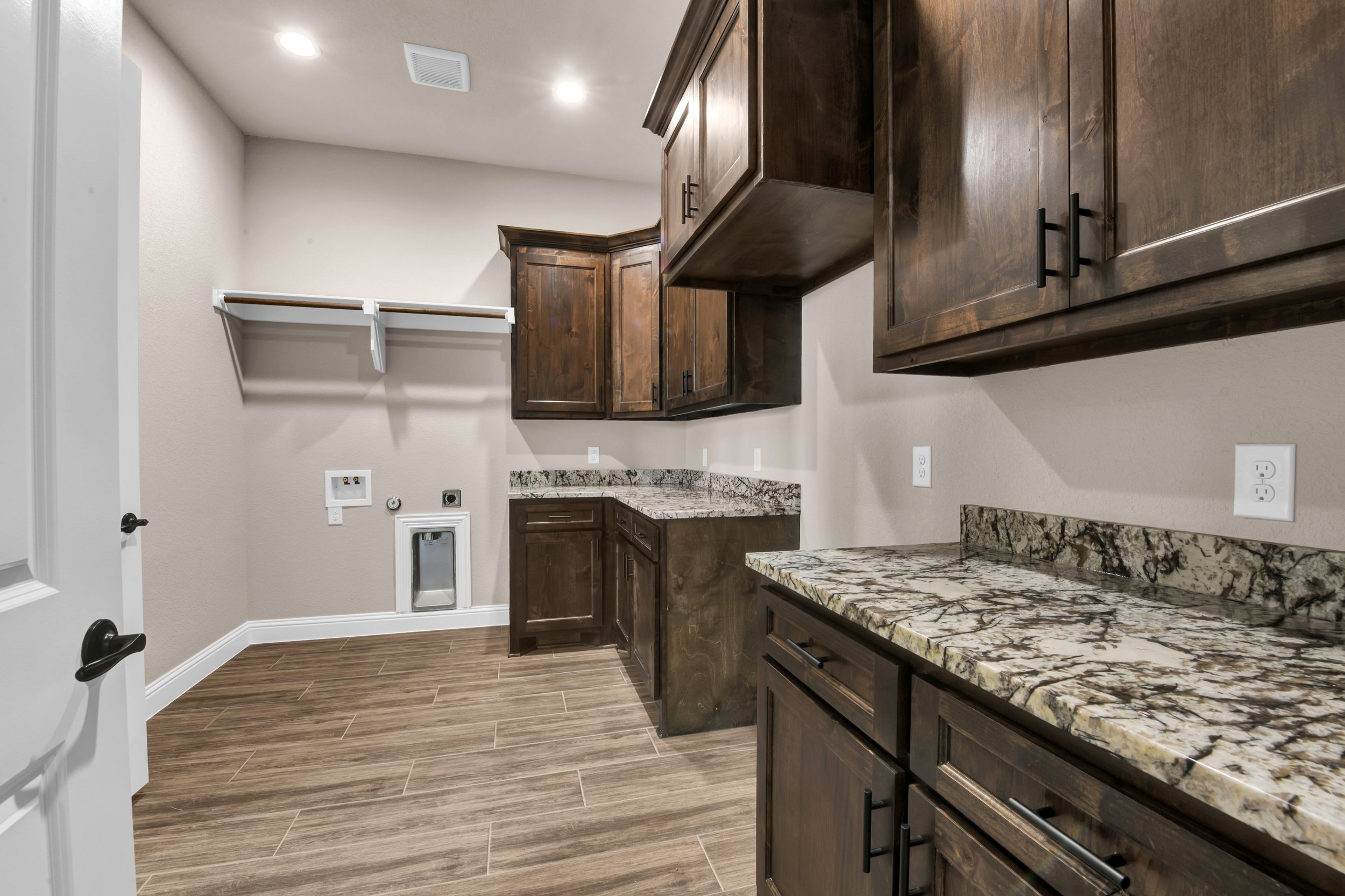 Empty laundry room with wooden cabinets, granite countertops, and wood-look tile flooring.