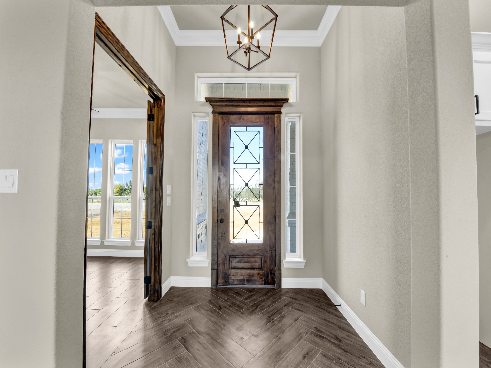 Entrance foyer with a wooden front door and adjacent windows, featuring light gray walls, white trim, and a geometric metal chandelier.