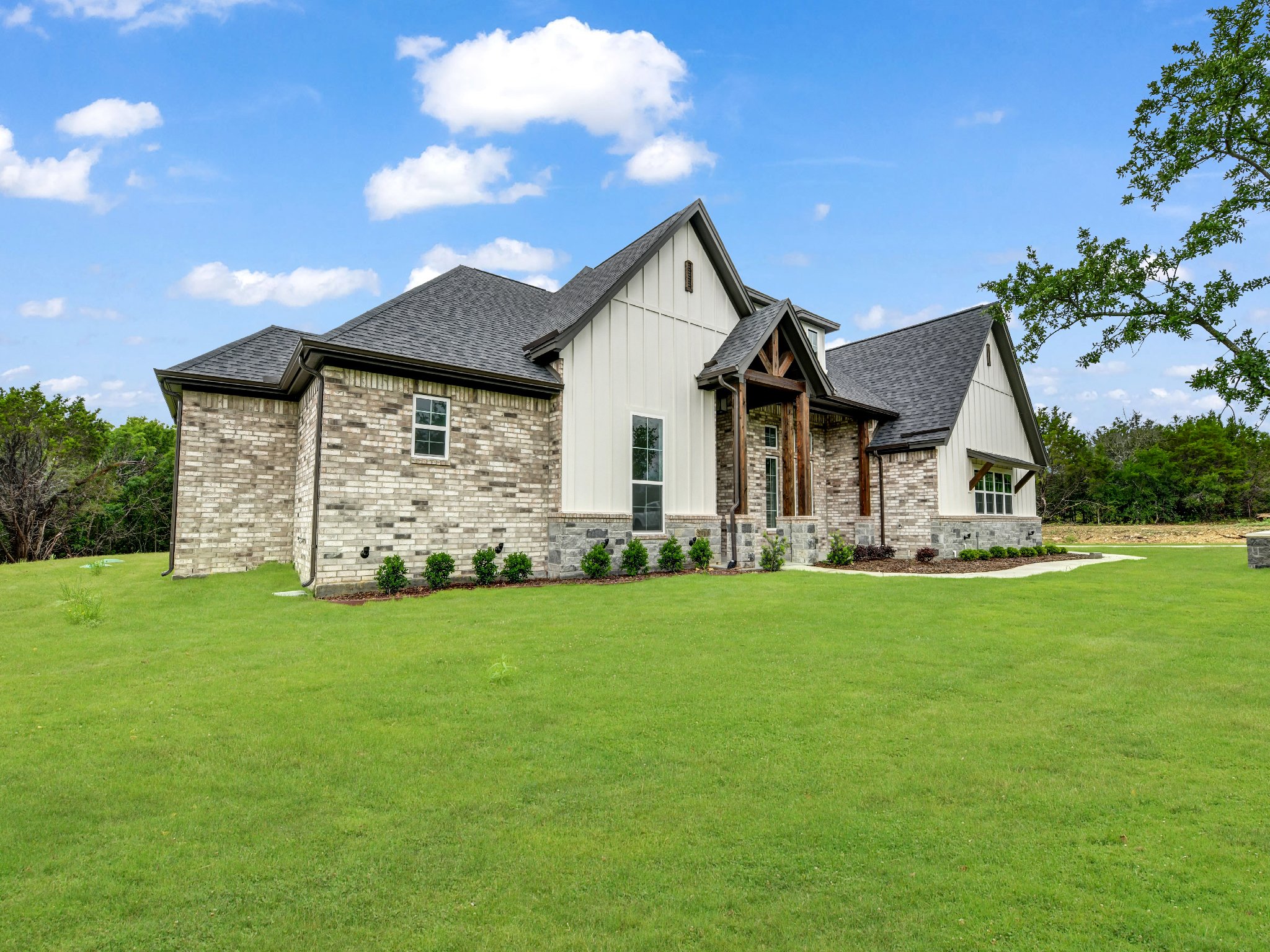 Newly constructed house with brick and siding exterior, gabled roof, front yard with green grass, and partly cloudy sky.