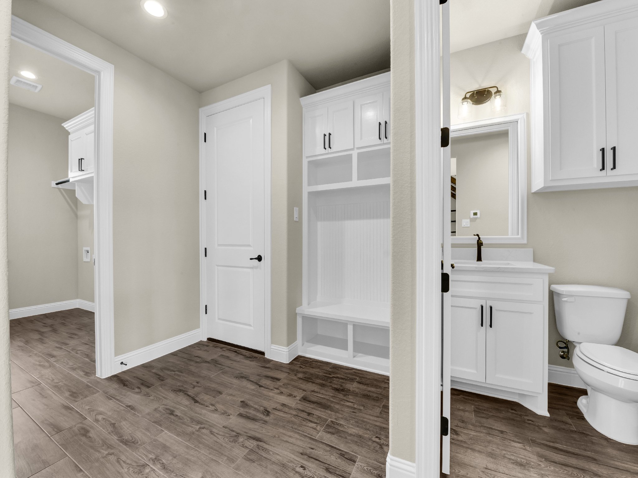 Interior view of a modern home with closet, bathroom vanity, and toilet, featuring white cabinets, beige walls, and wood-like flooring.