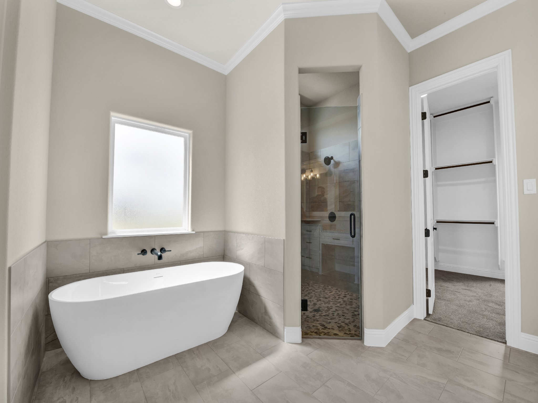 Bathroom with a white bathtub, a walk-in shower with glass door and pebble floor, and an empty closet