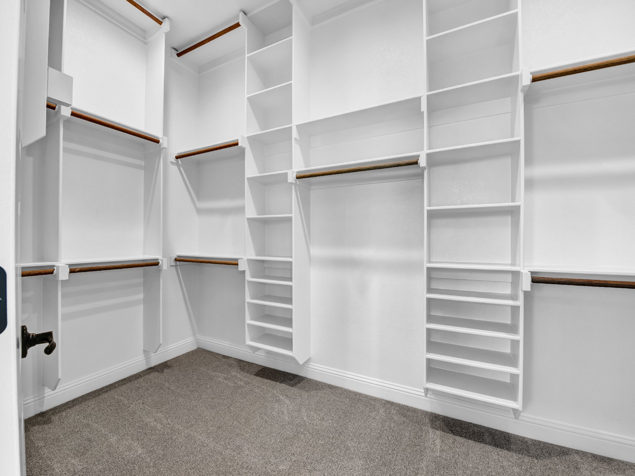 Empty walk-in closet with white shelving and wood hanging rods.