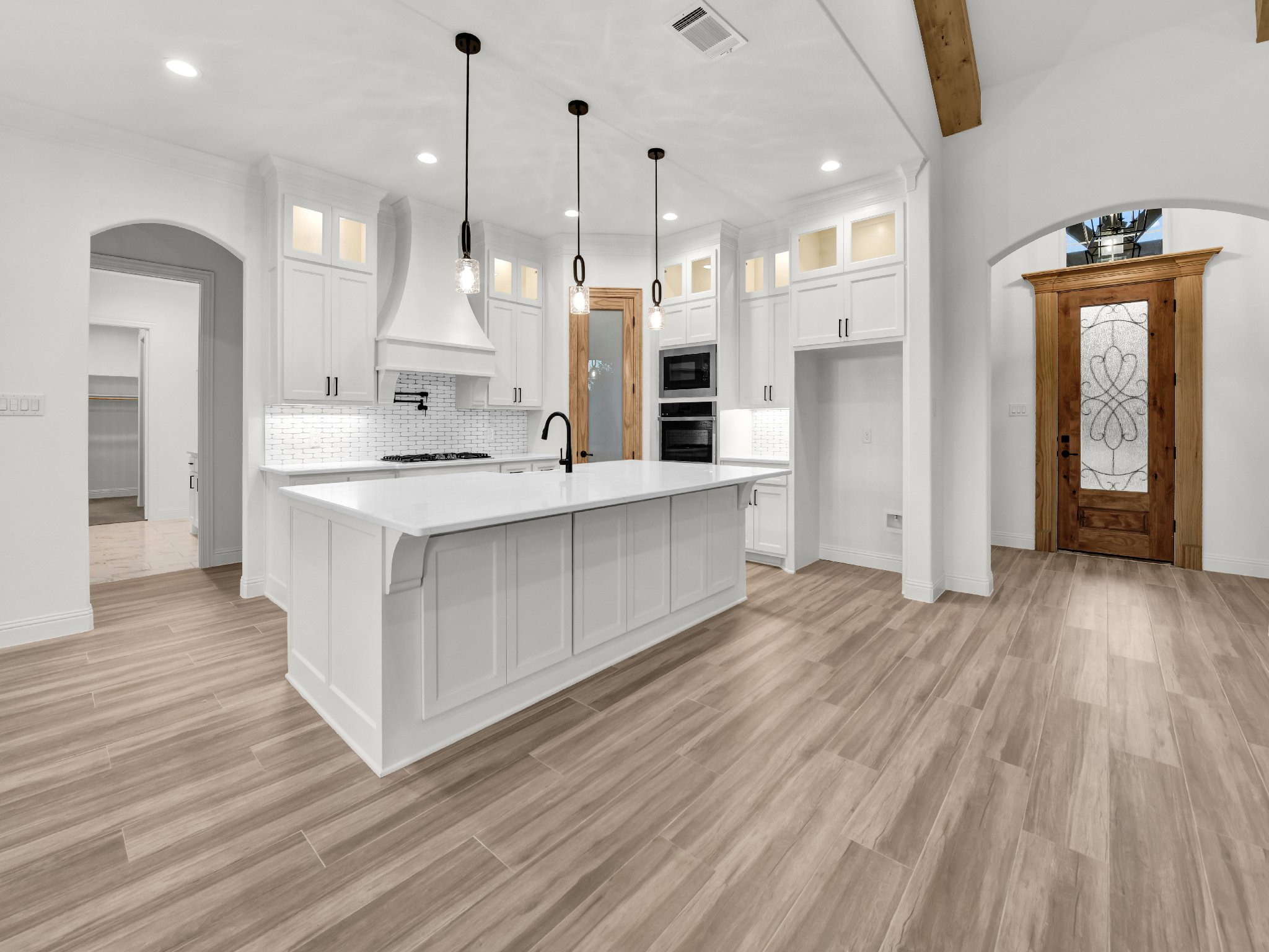Modern white kitchen with island, pendant lights, white cabinetry, and wooden door, hardwood flooring.
