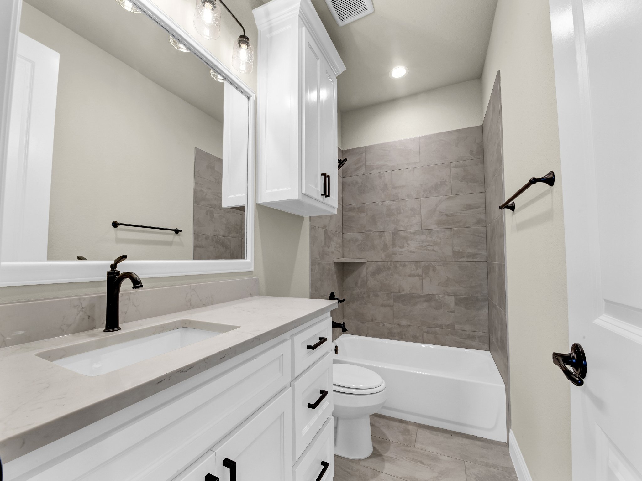 Modern bathroom with white vanity, black fixtures, large mirror, tiled shower with built-in shelf, and beige walls.