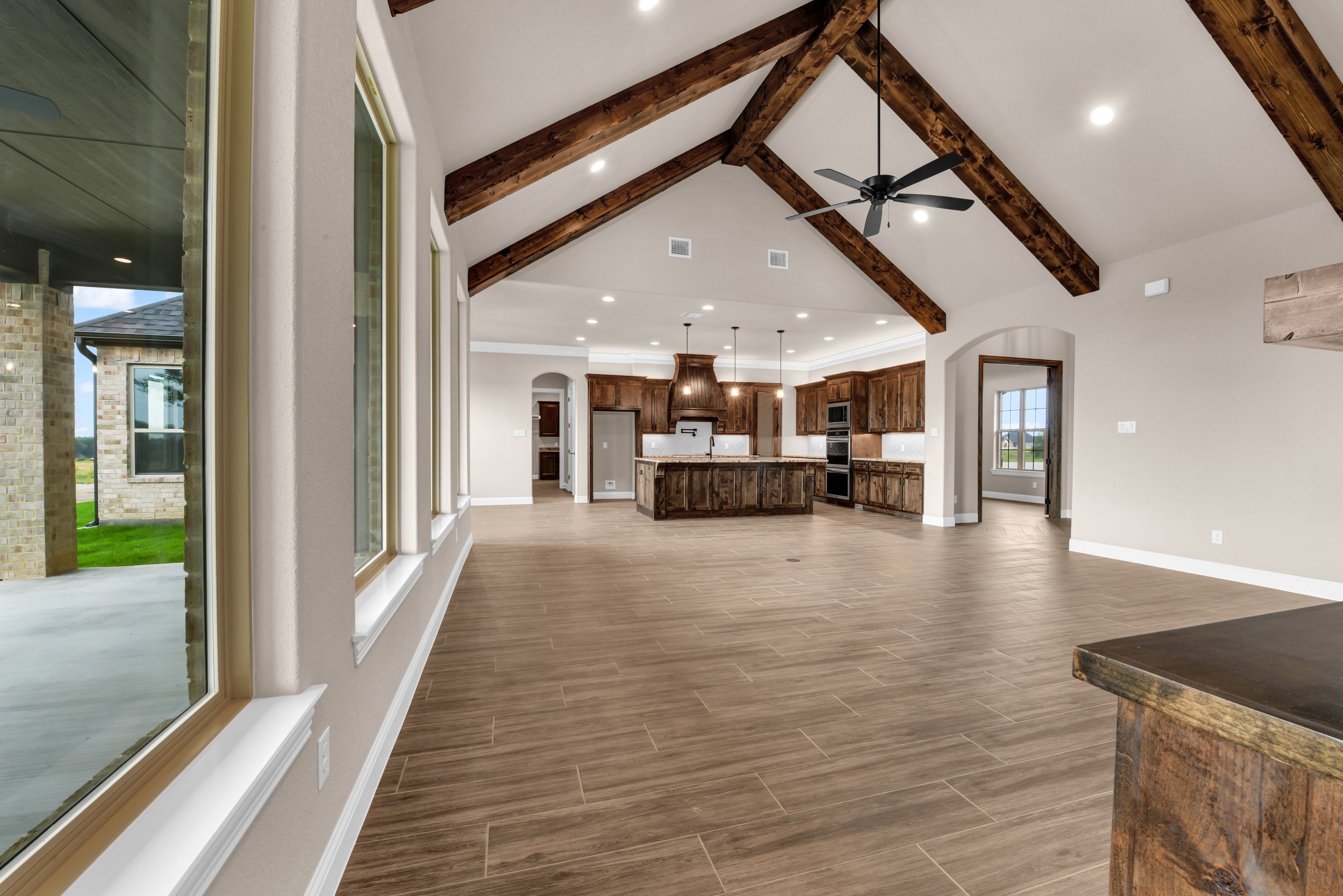 Modern open-concept kitchen and living area with wood accents, large windows, and a vaulted ceiling with dark wooden beams.