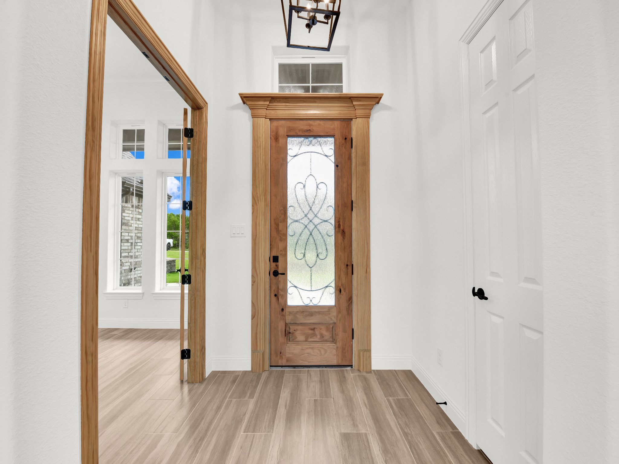 Entryway with wooden front door featuring decorative glass, side window, wooden doorframes, and adjacent interior doors with black handles.