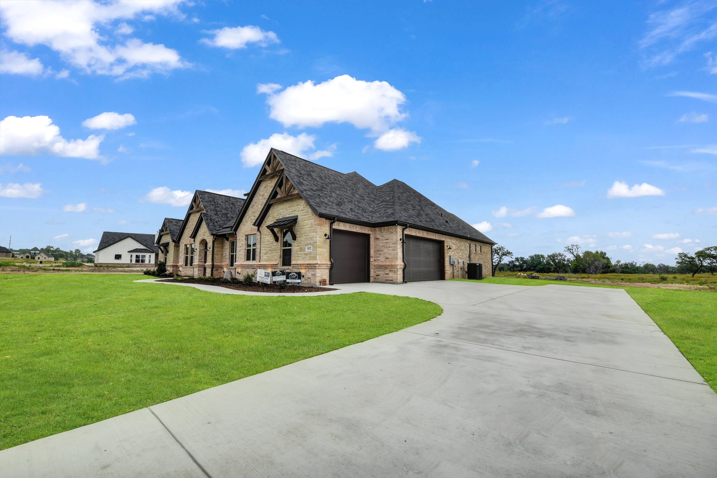 A new brick house with three garage doors, surrounded by green lawn and blue sky with clouds.