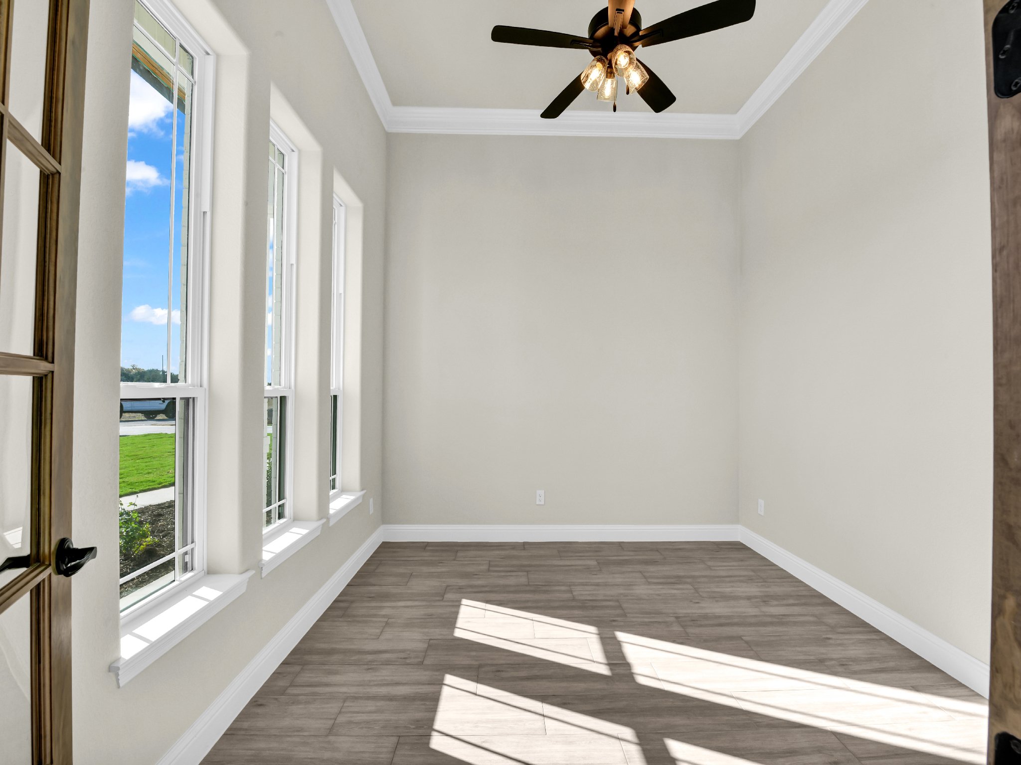 Empty room with four large windows, a ceiling fan, and light wood flooring.