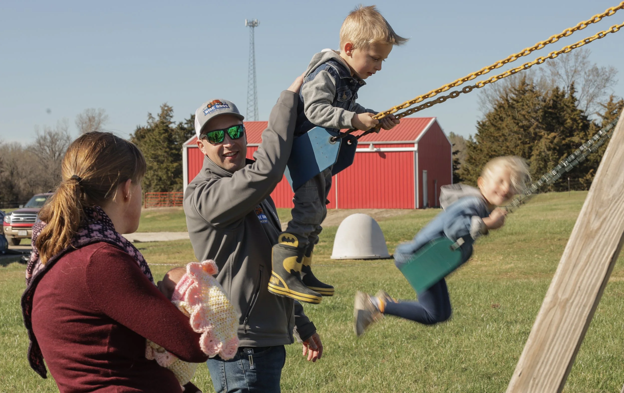 From left: Elaine, Adelaide, two weeks, watch Harrison as he pushes Lewis, 4, and Miriam, 5, on a swing on March 20, 2025, at their home in Fulton, Mo. The kids have already shown an interest in their dad’s work, playing with toy tractors and farm eq