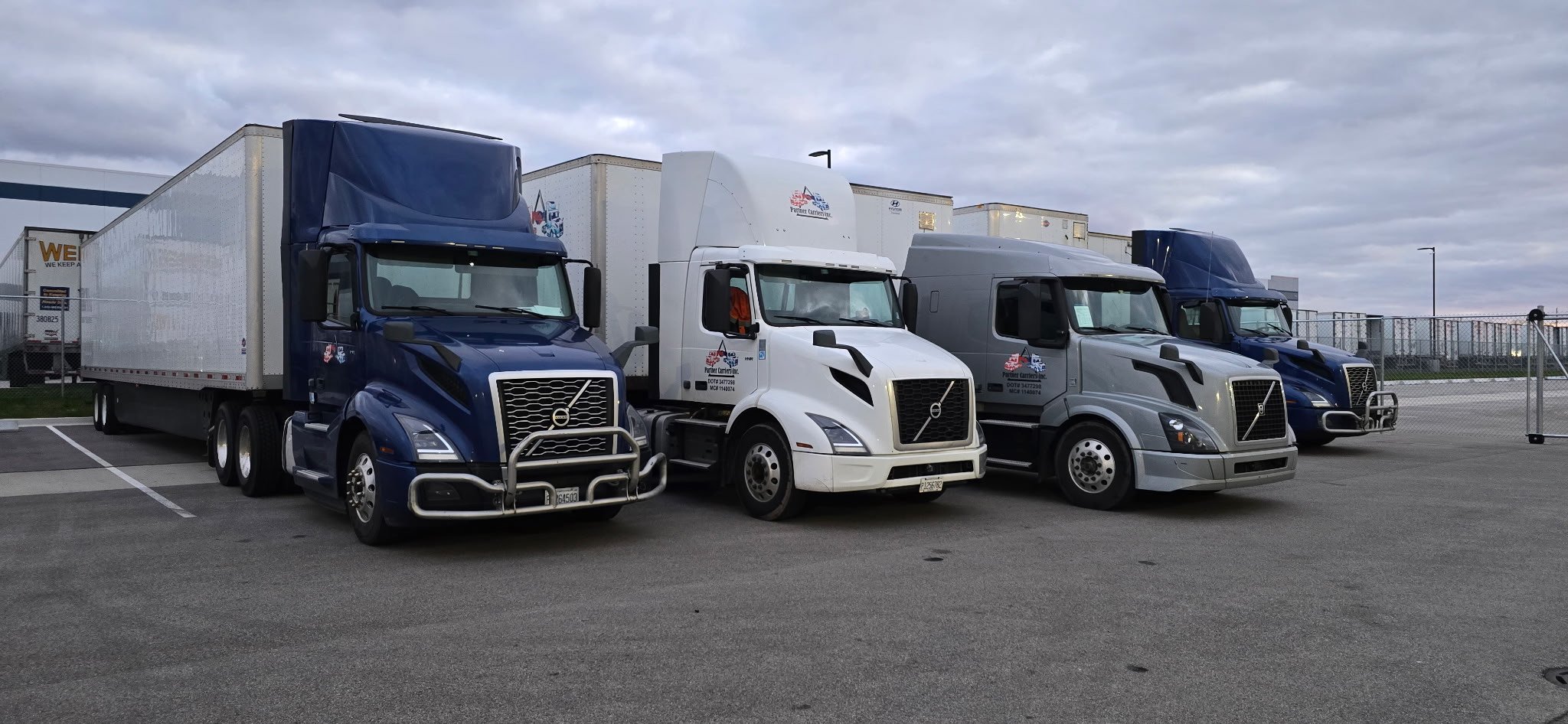 Four Partner Carriers Inc. semi-trucks parked in a lot during cloudy weather.