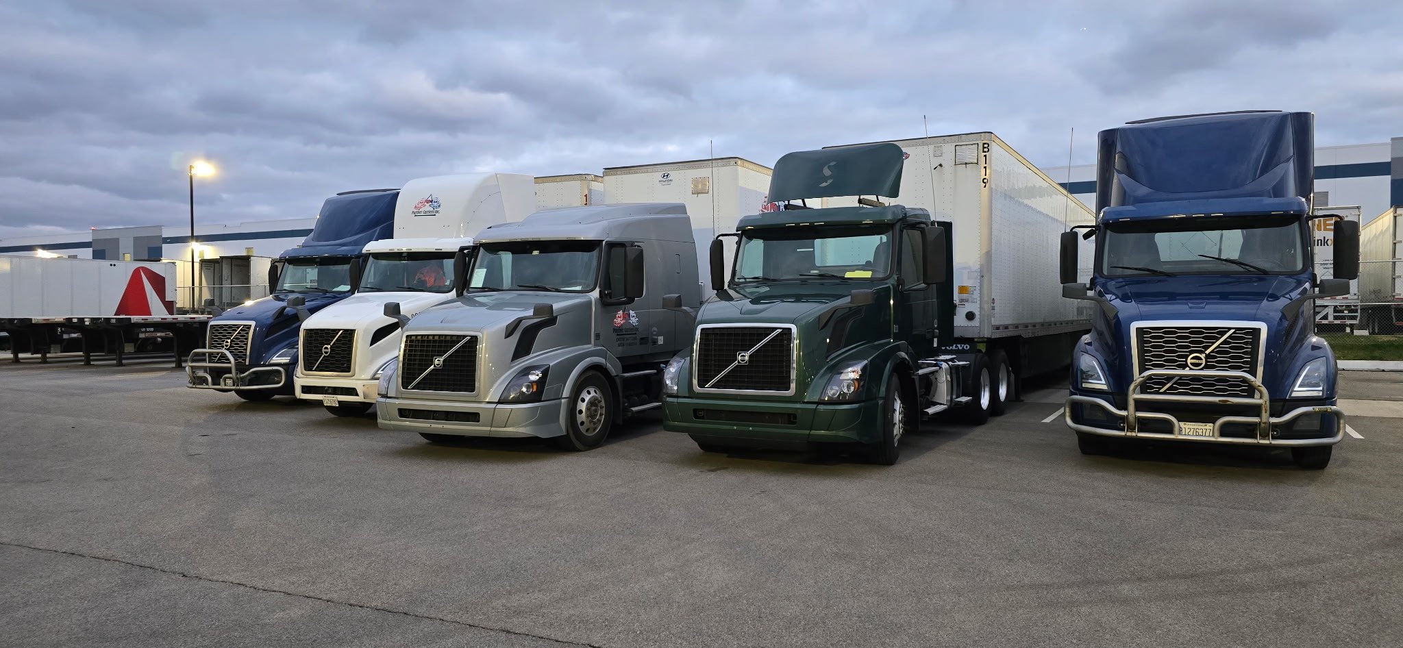 Lineup of Partner Carriers Inc. Volvo semi-trucks with trailers in a parking lot under cloudy sky.