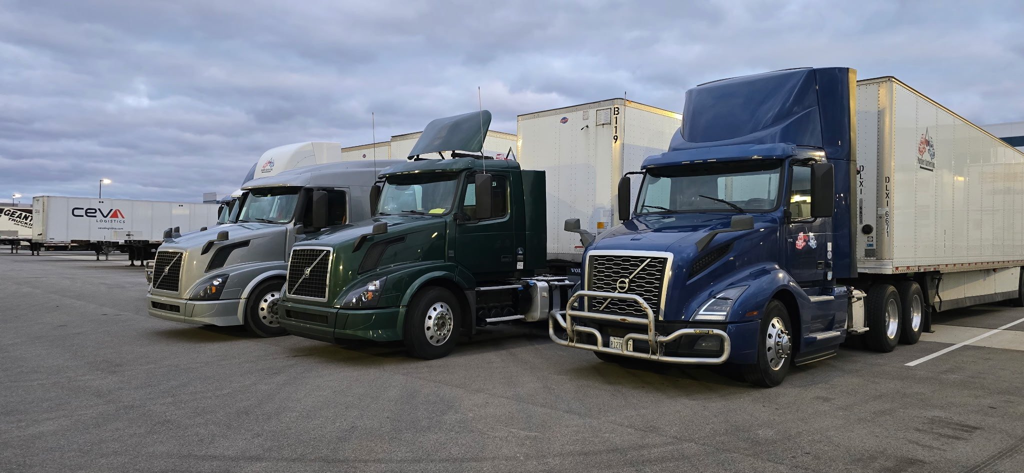 Three Partner Carriers Inc. Volvo semi-trucks parked in a lot with trailers in the background.
