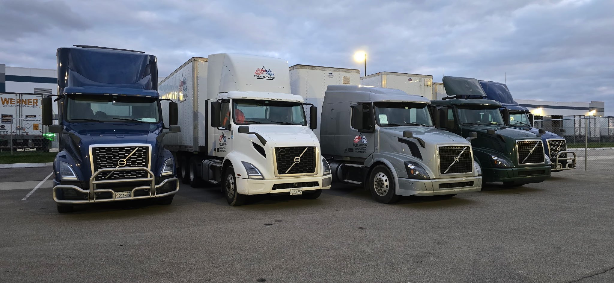 Four Partner Carriers Inc. Volvo semi-trucks parked in a row at a truck yard.