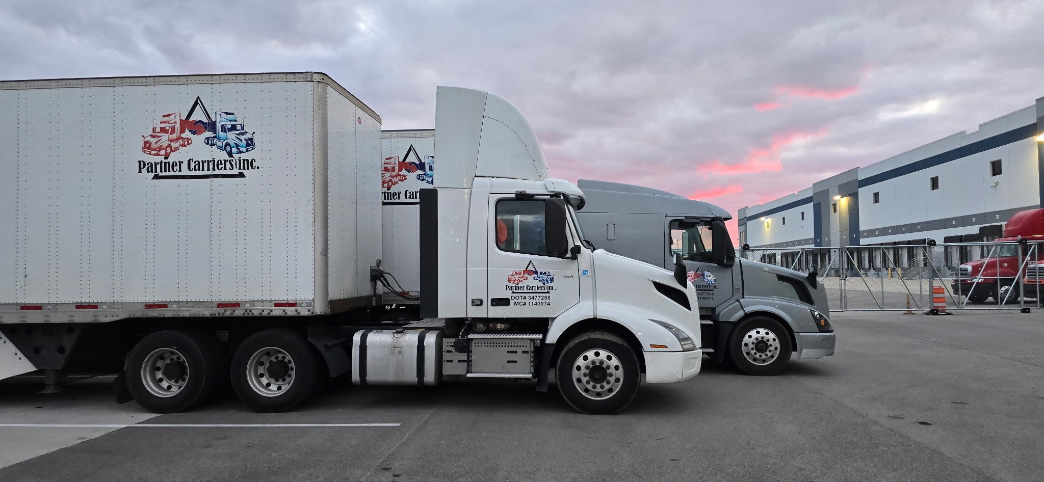 Two semi-trucks with "Partner Carriers Inc." logo parked in an industrial area during sunset.