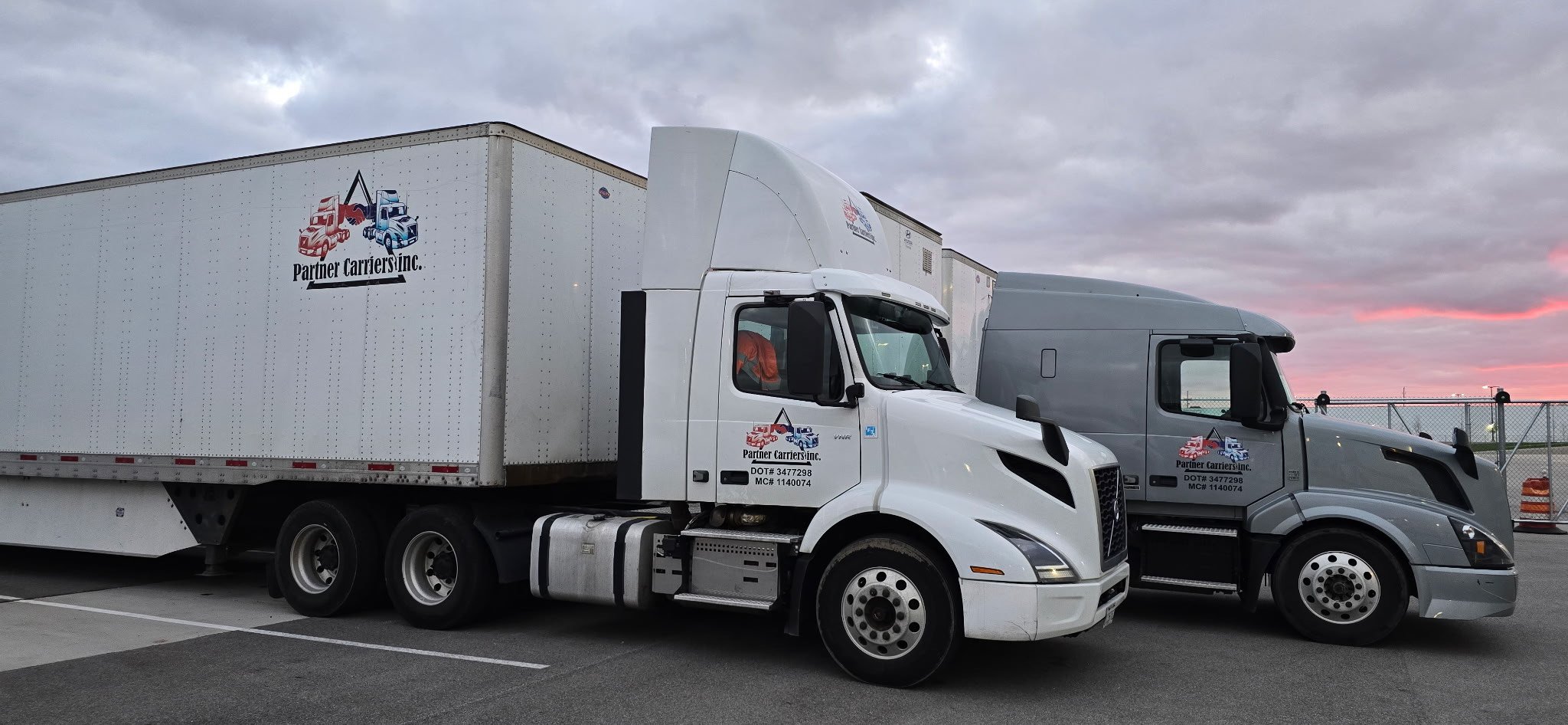Two trucks from Partner Carriers Inc. parked side by side under a cloudy sky.