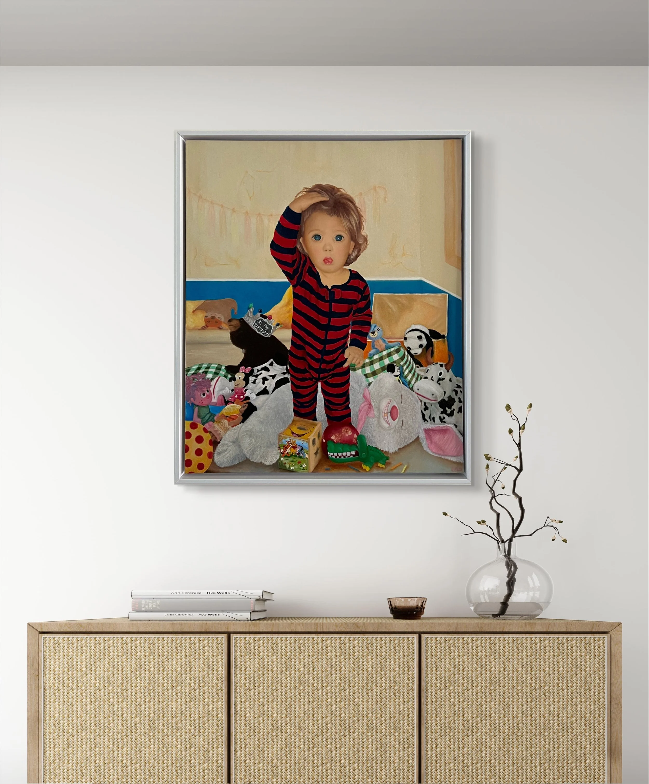 A baby in red and blue striped overalls standing surrounded by tossed plush toys, with a wall and curtains in the background.