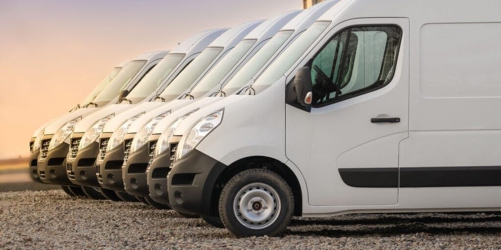 Row of white commercial vans parked on gravel with sunrise background.