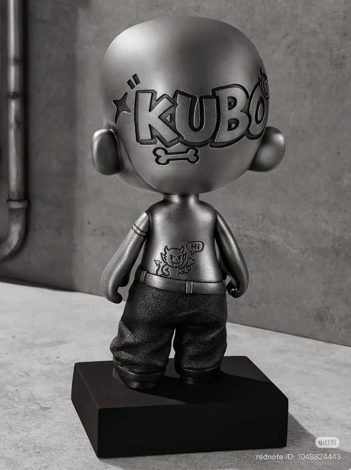 Back view of KUBO: TIN ME 200%, with the oversized “KUBO” logo engraved across the head.