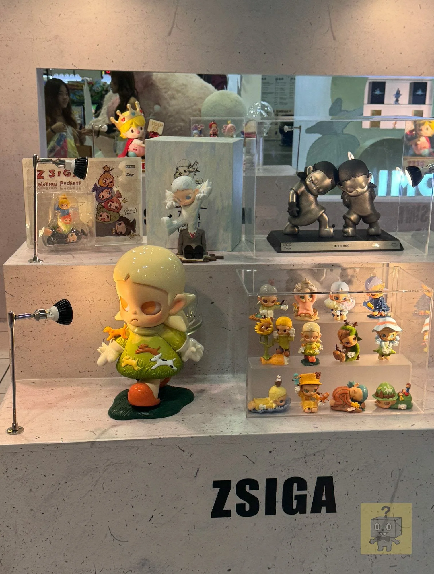 A Zsiga display case at POP TOY SHOW Singapore, with multiple boxed items and small figures on acrylic risers; “ZSIGA” is printed in large letters on the front of the display.