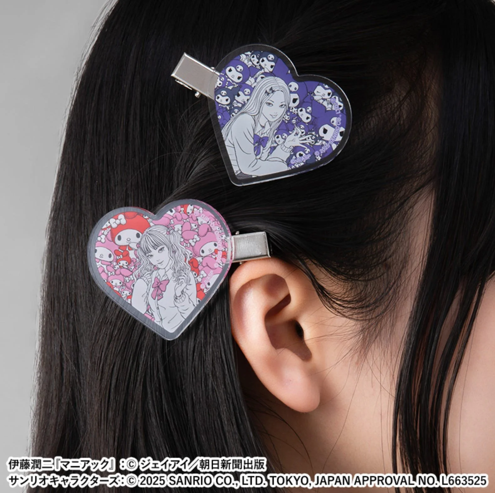 Two heart-shaped acrylic hair clips worn near an ear—one pink and one purple—each printed with Tomie artwork and Sanrio motifs.