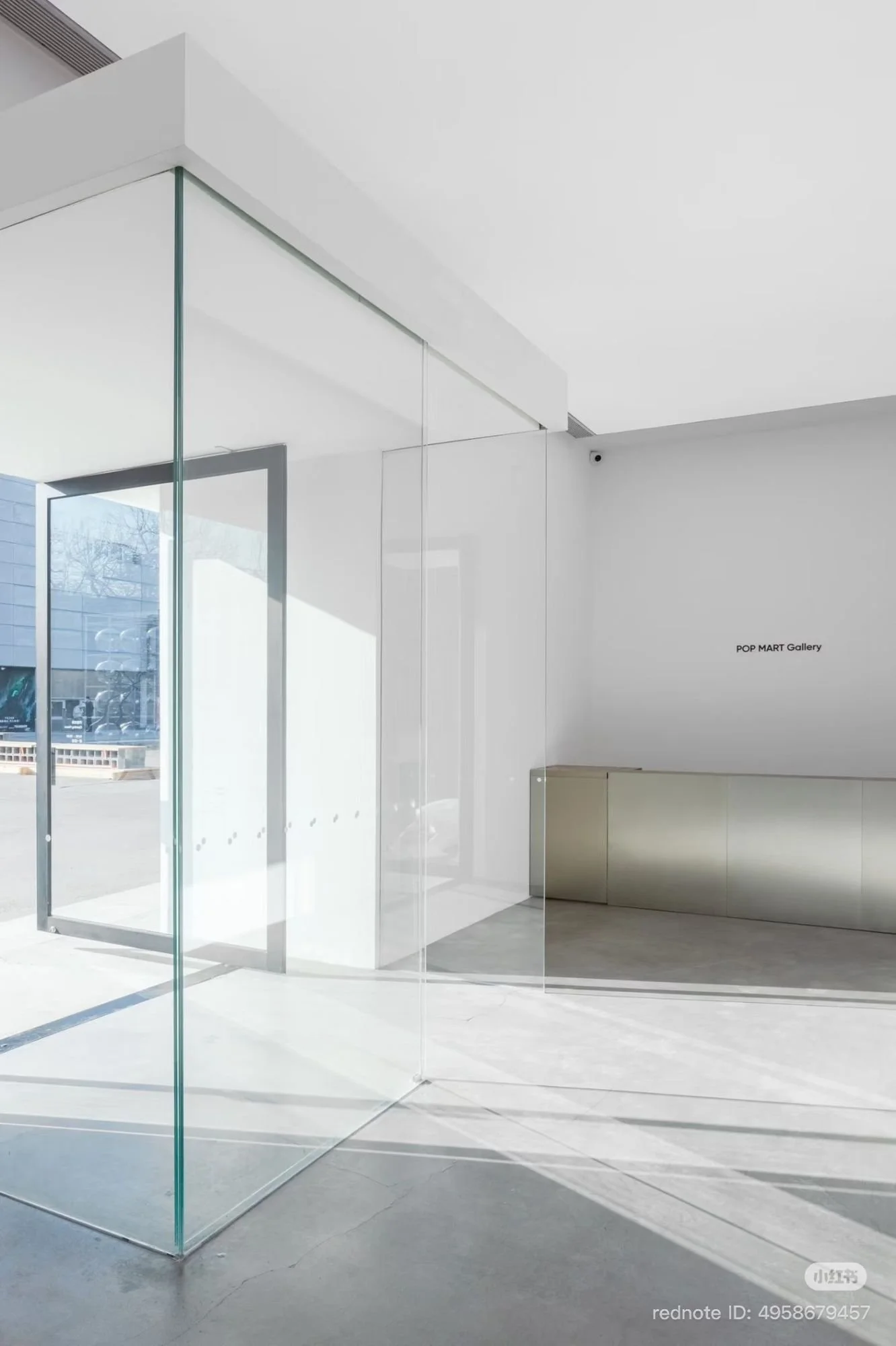 Bright interior lobby with glass walls and a low reception desk; “POP MART Gallery” appears on the far wall as sunlight cuts across the floor.