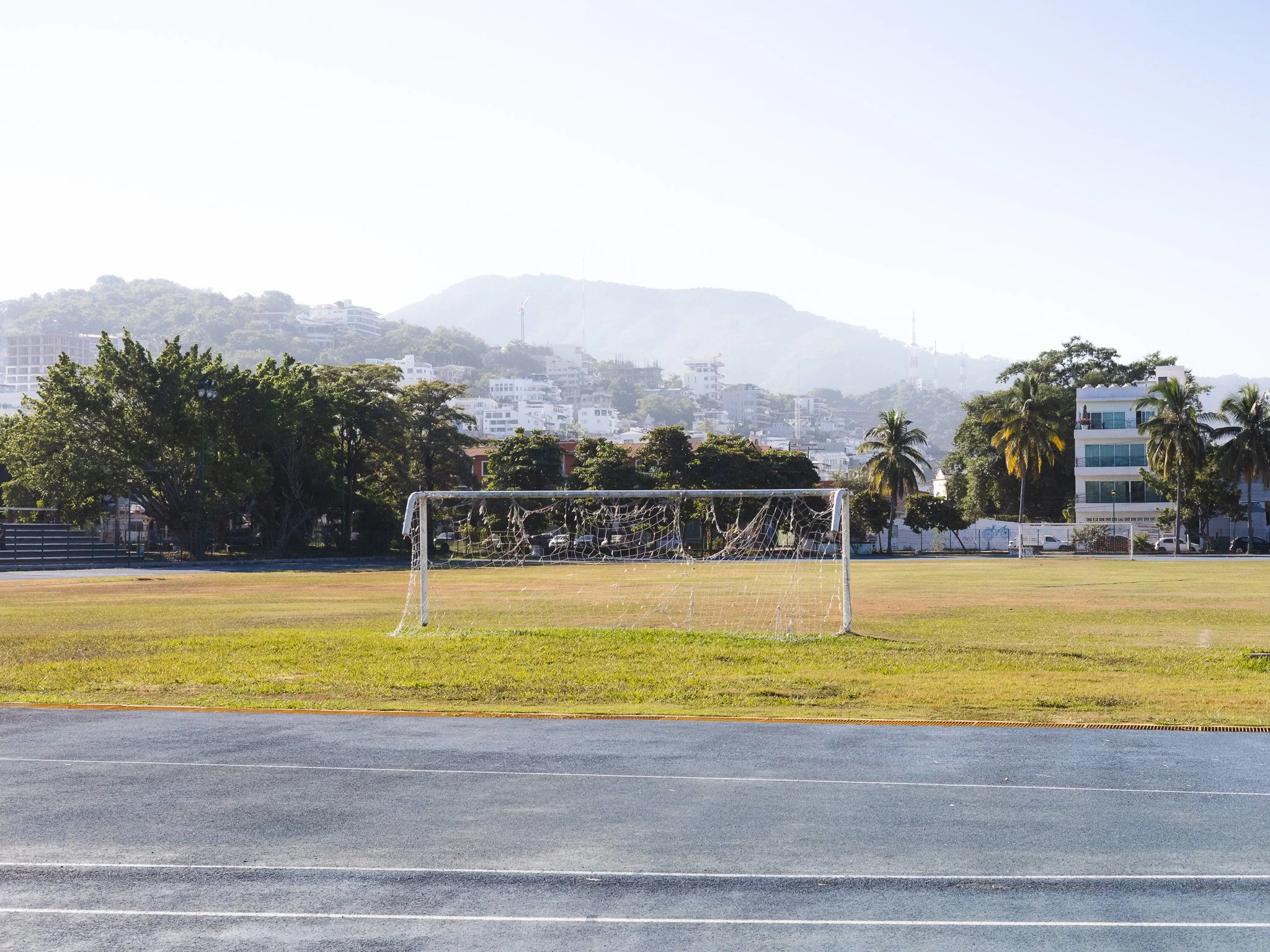 Empty soccer goal on a grassy field with mountains and modern buildings in the background