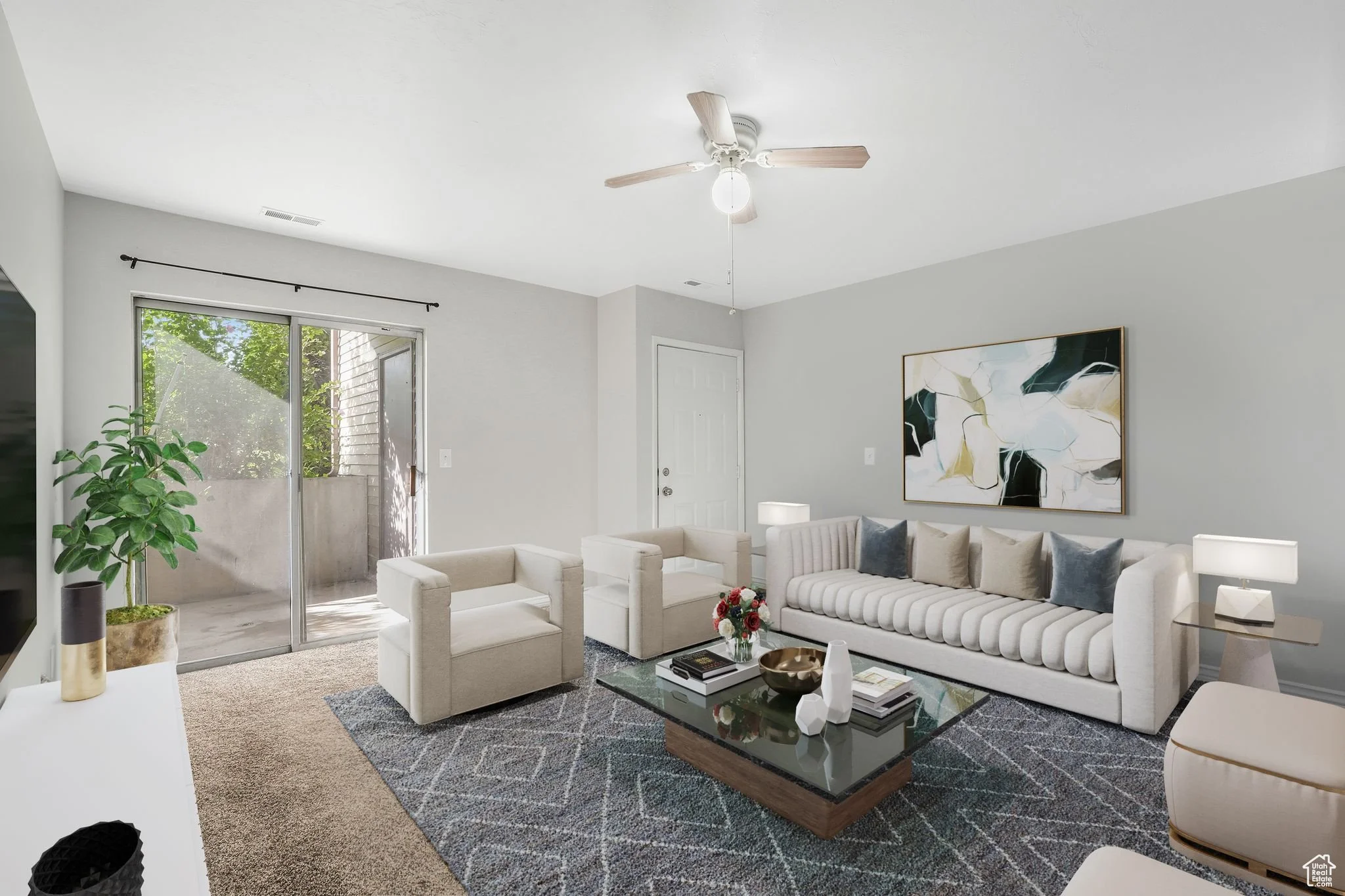 Small beige house with a front porch, white door, and two windows. The yard has green grass and trees, with mountains in the background.