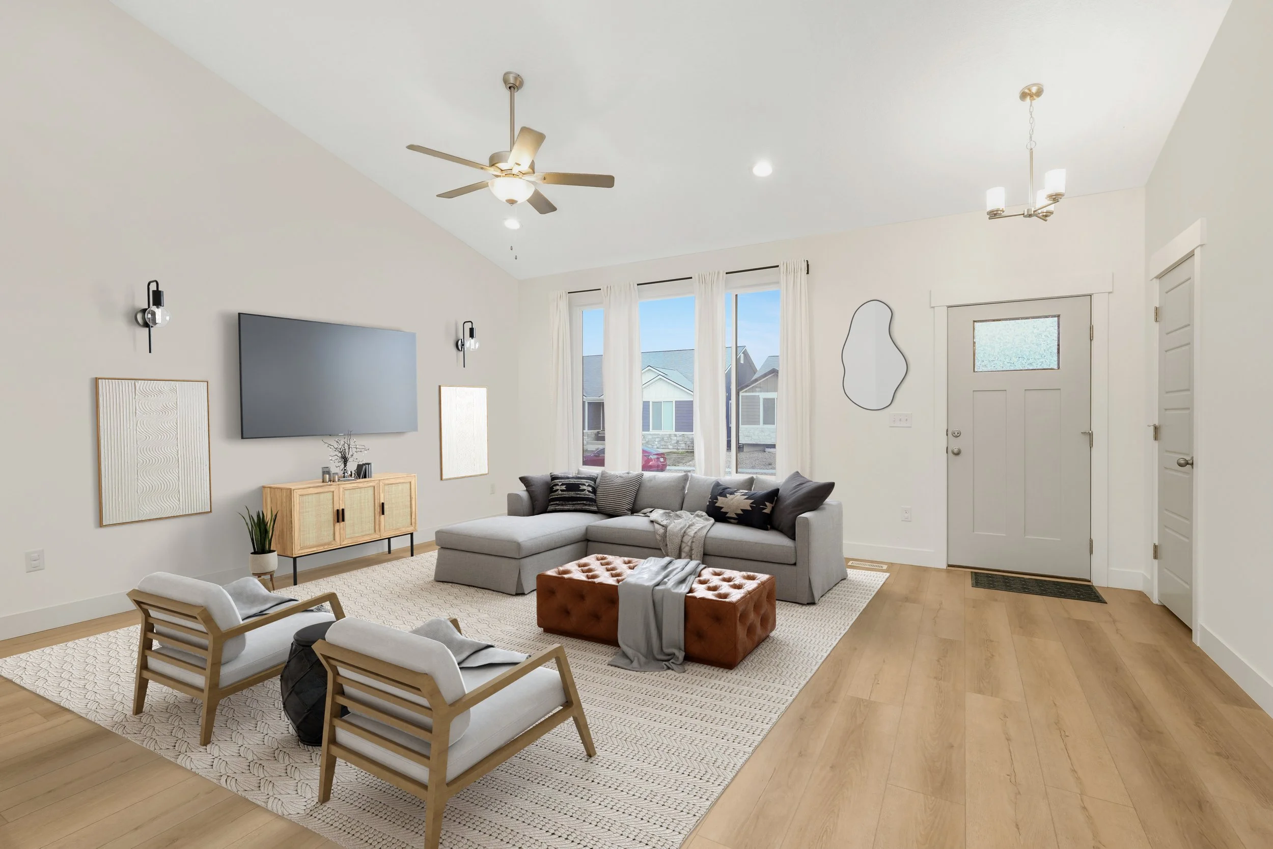 Modern living room with gray sectional sofa, wooden armchairs, wall-mounted TV, ceiling fan, and light fixtures. Tan wooden floor and door, geometric mirror, and large windows with sheer curtains.