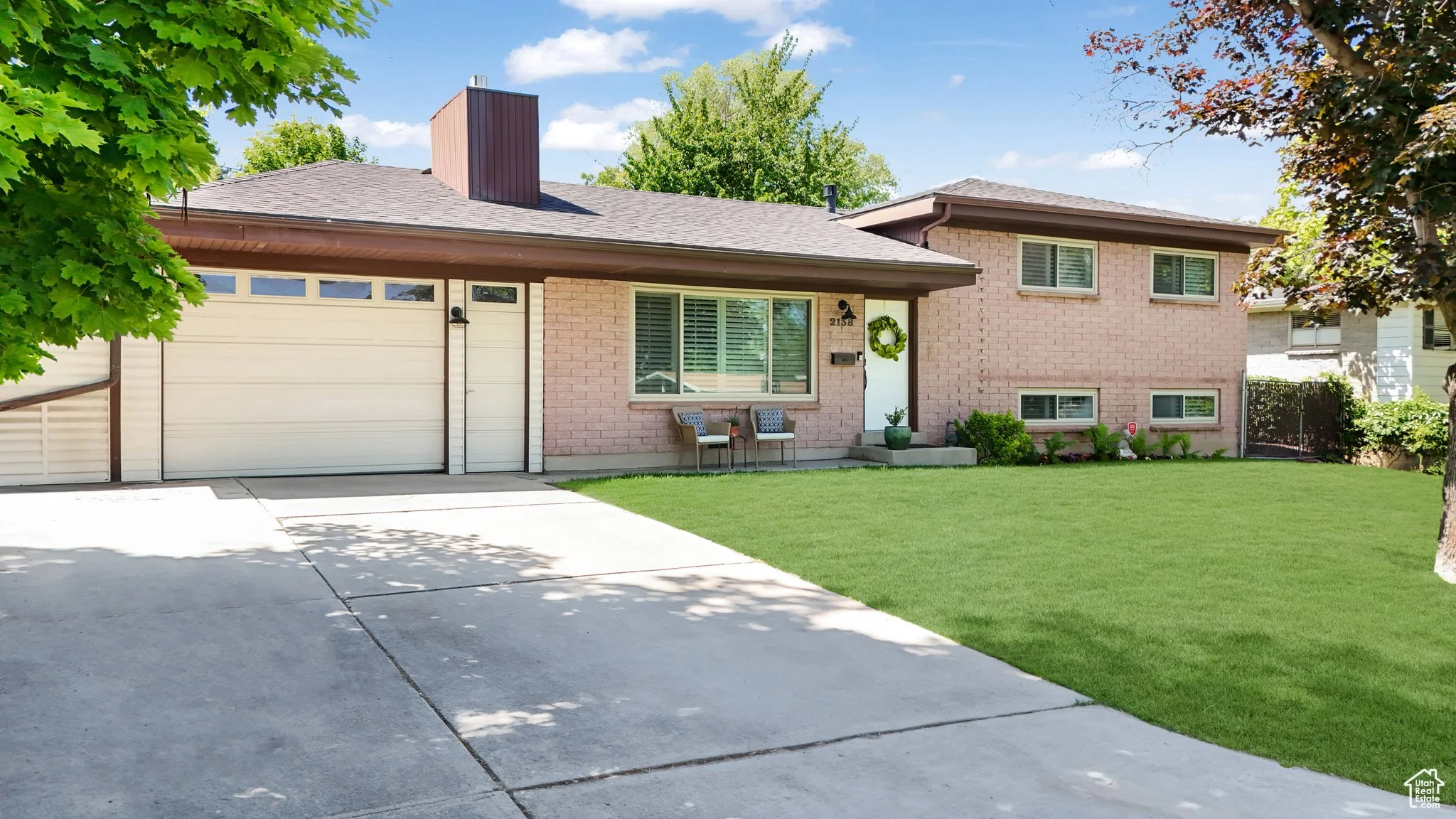 Suburban brick house with a two-car garage, front lawn, and a tree on the left side.