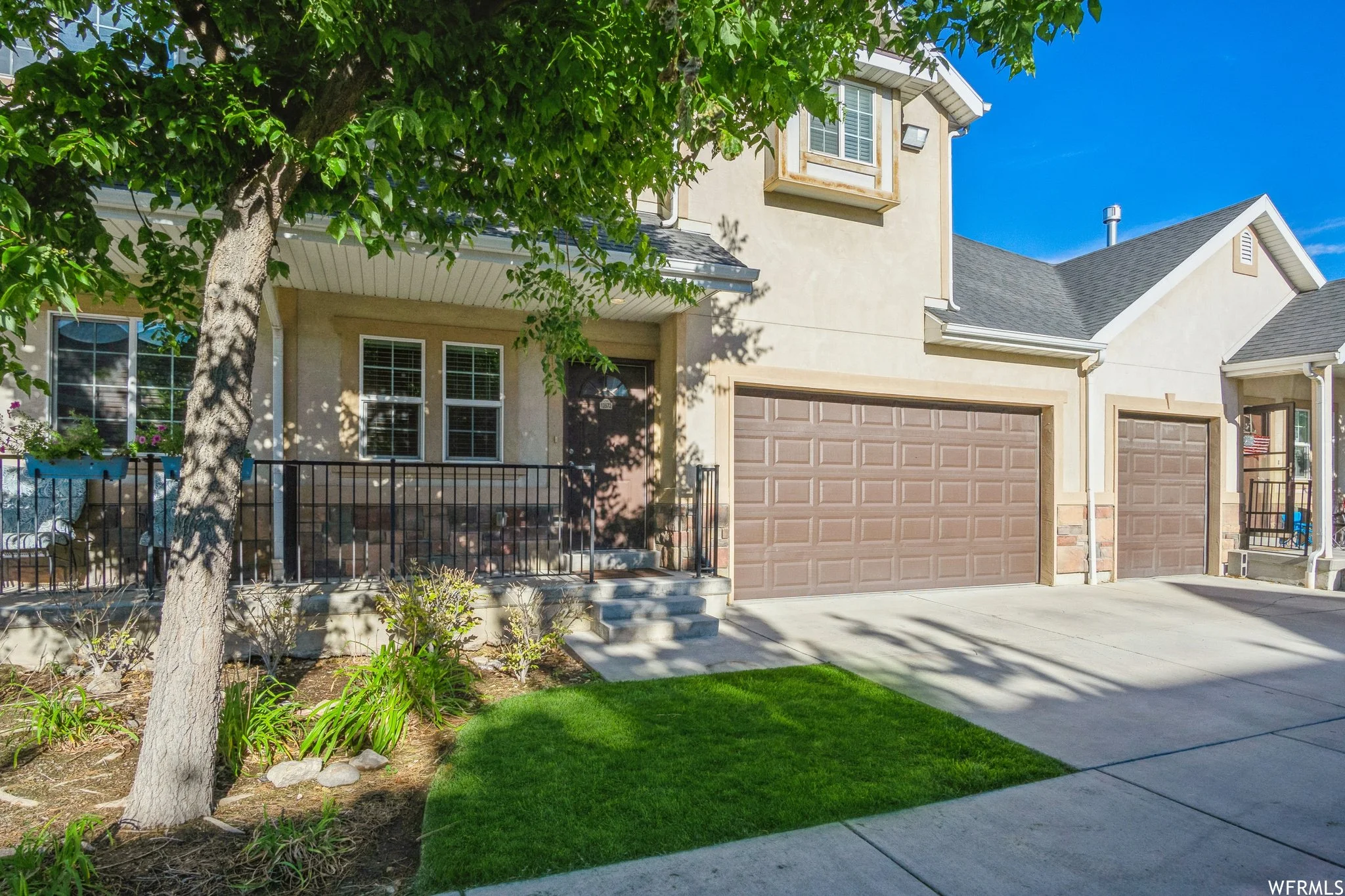 Exterior view of a suburban house with a double garage, a tree, and a small front yard.