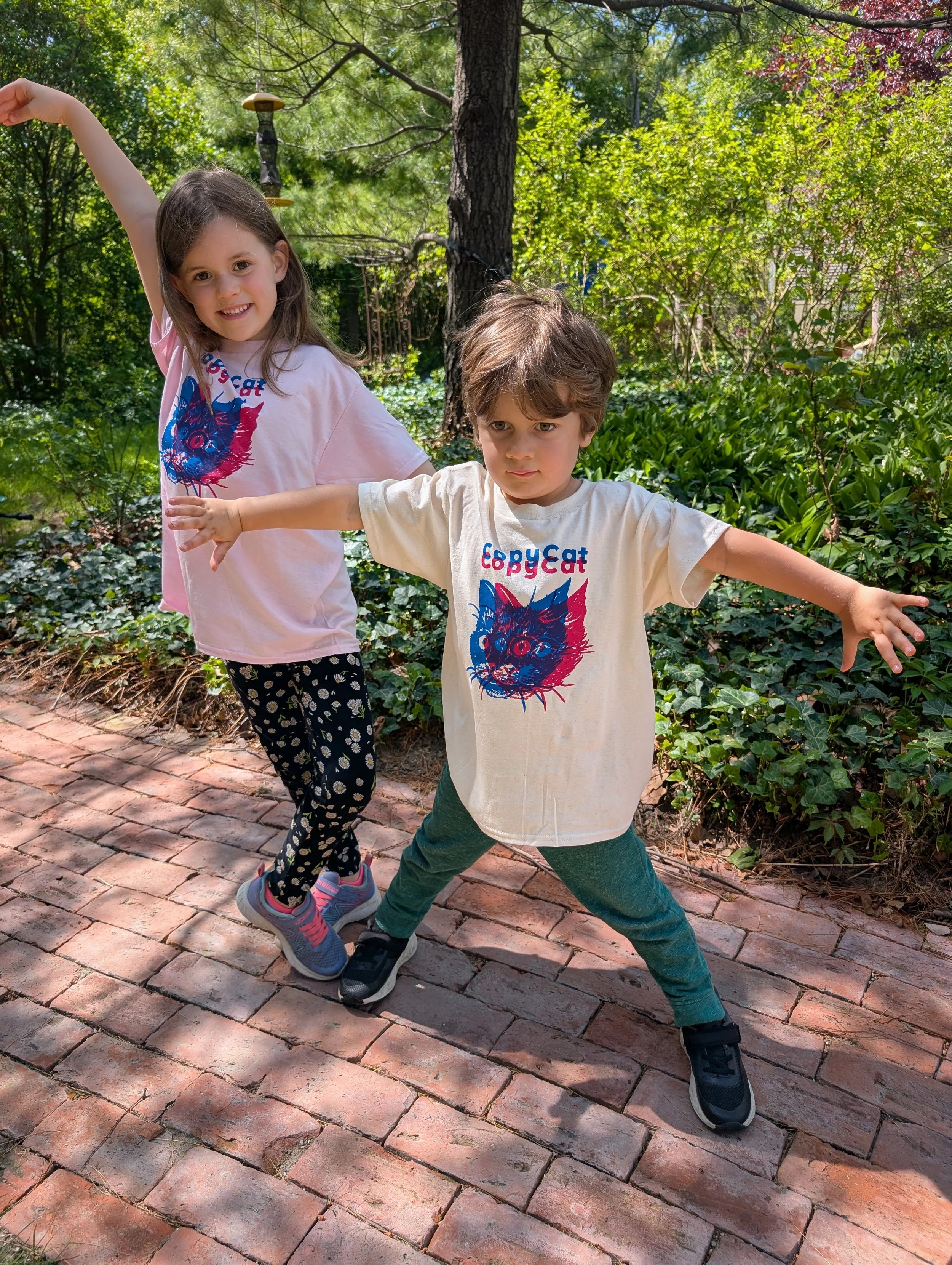 Two children wearing CopyCat t-shirts, which feature illustrated cat heads printed in pink and blue.