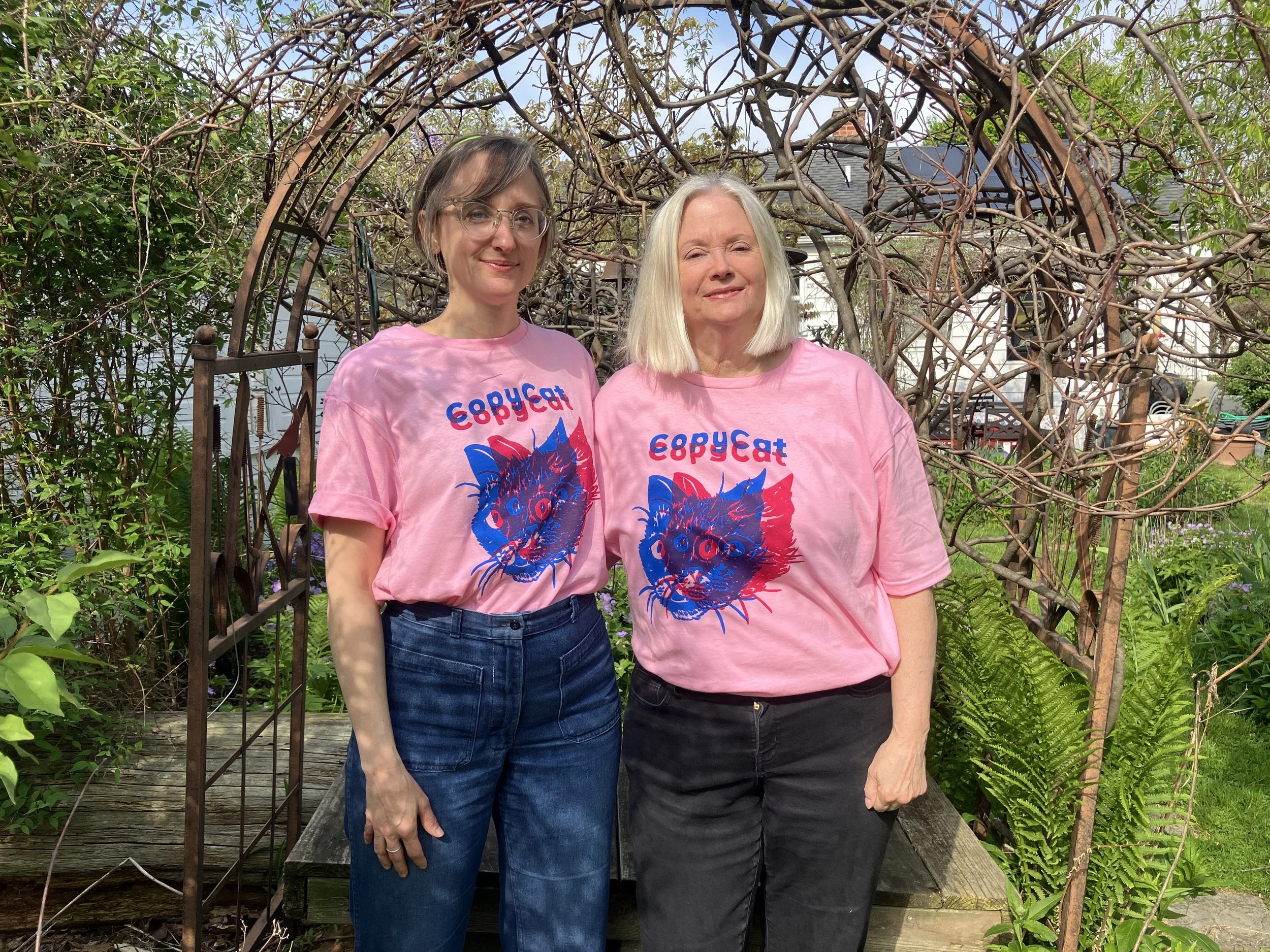 Two people wearing pink CopyCat t-shirts, which feature illustrated cat heads printed in pink and blue.