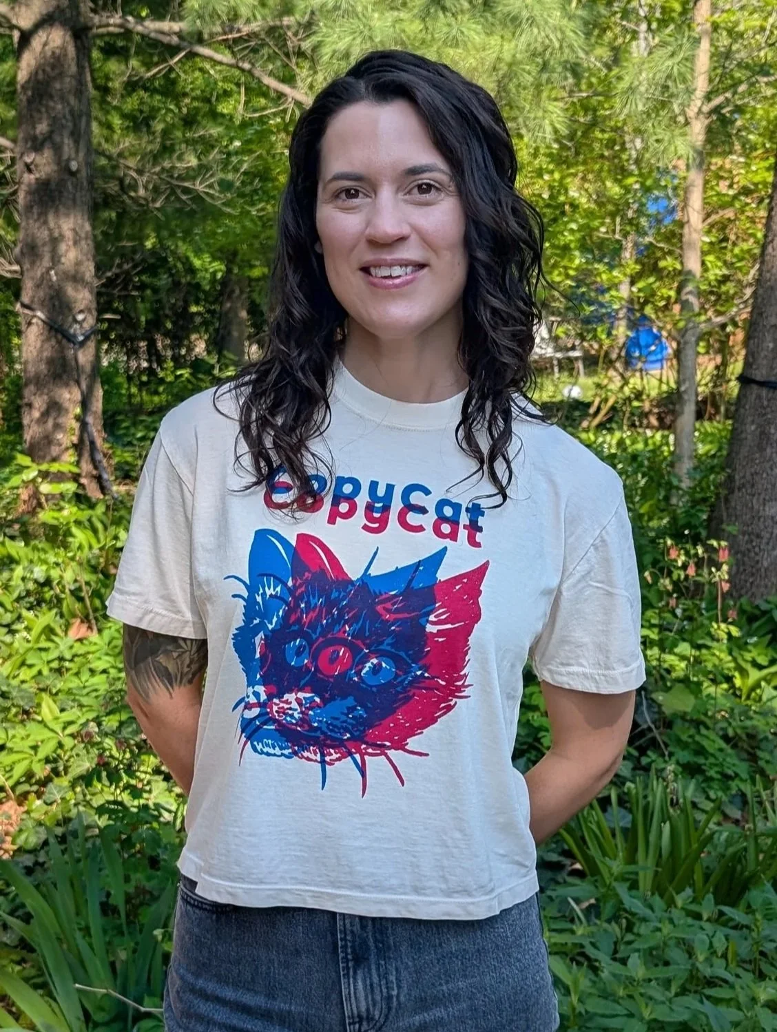 A person wearing an off-white CopyCat t-shirt in a boxy cut; the t-shirt features an illustrated cat head printed in pink and blue.