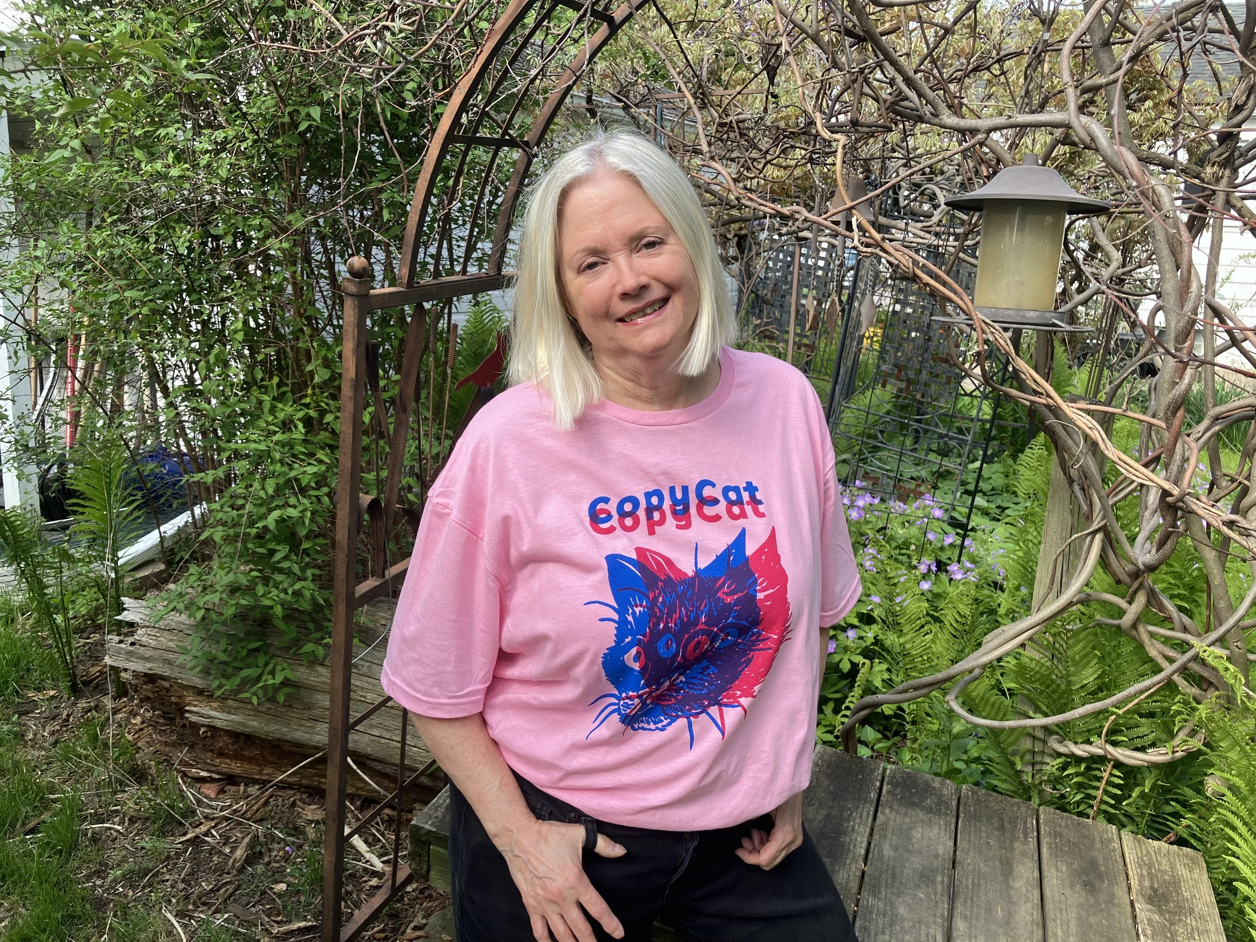 A person wearing a pink CopyCat t-shirt, which features overlapping illustrated cat heads in pink and blue.