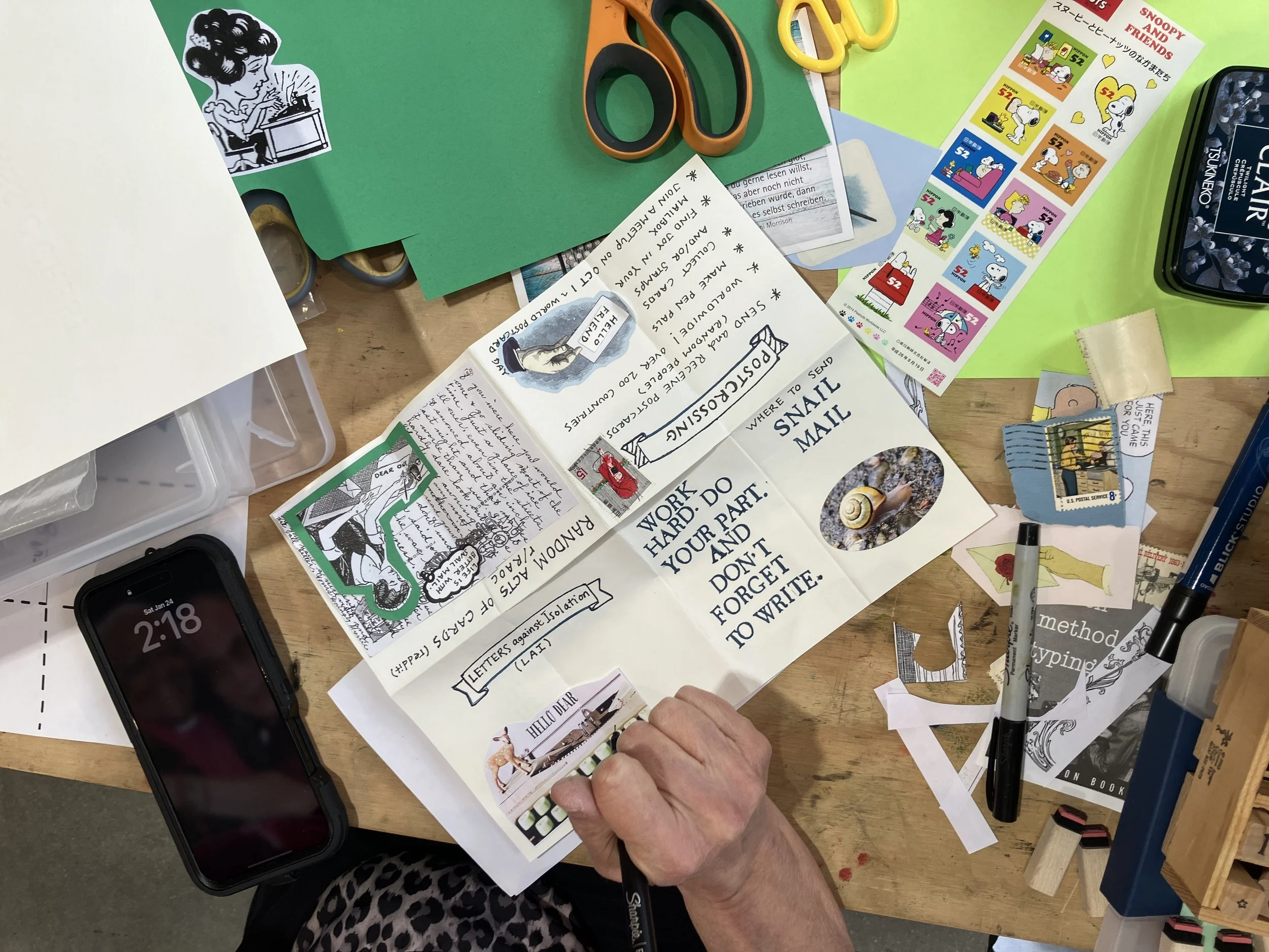 An overhead view of a person working on their zine, with scissors and glue and collage materials around them.