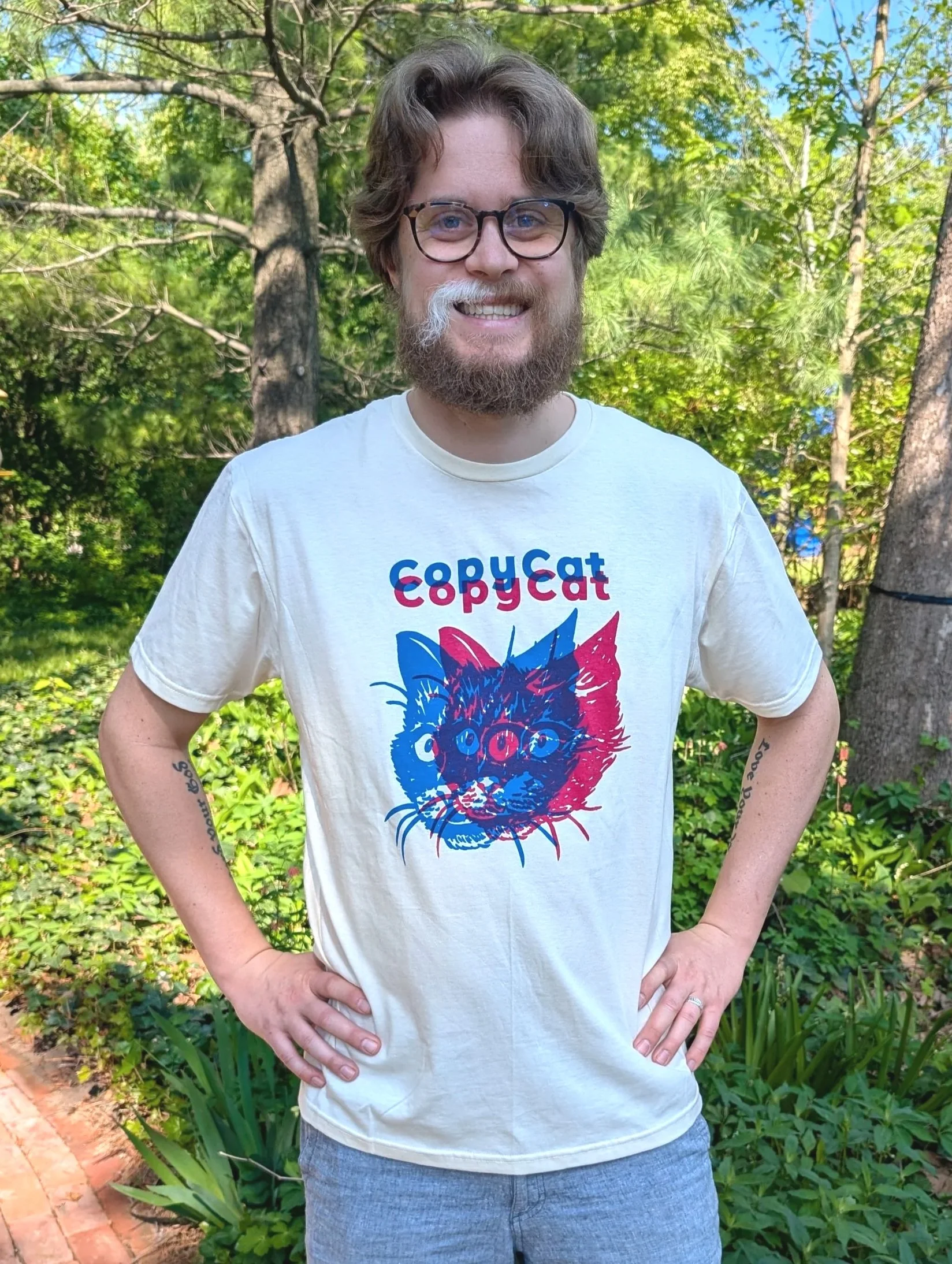 A person wearing an off-white CopyCat t-shirt, which features an illustrated cat head printed in pink and blue.