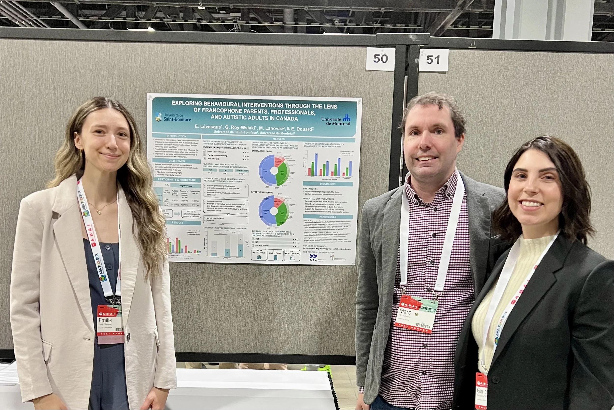 Trois personnes posant devant une affiche de recherche lors d'une conférence. La femme à gauche porte un blazer beige et une chemise noire, la femme à droite porte une veste noire et une chemise crème, l'homme au centre porte une veste grise et une chemise à carreaux rouge et blanc. Tous portent des badges d'identification.