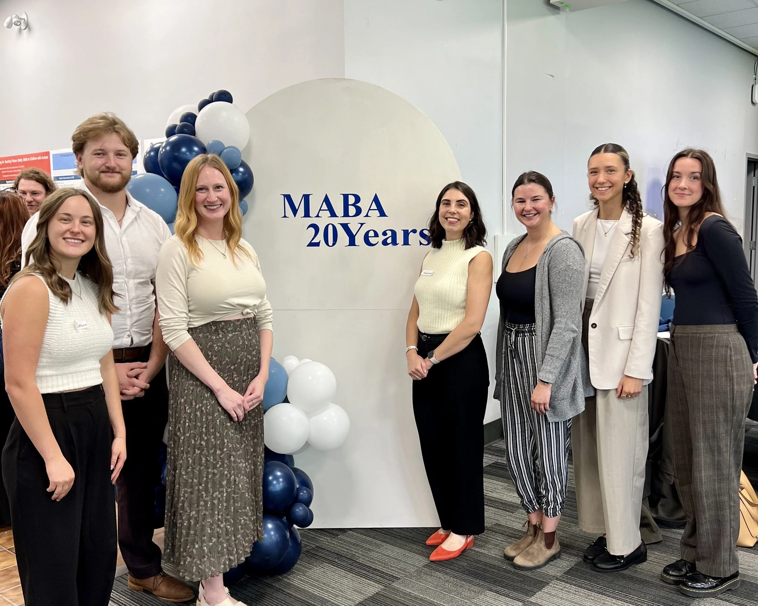 Groupe de huit personnes posant devant un panneau indiquant 'MABA 20 Years' lors d'une célébration.