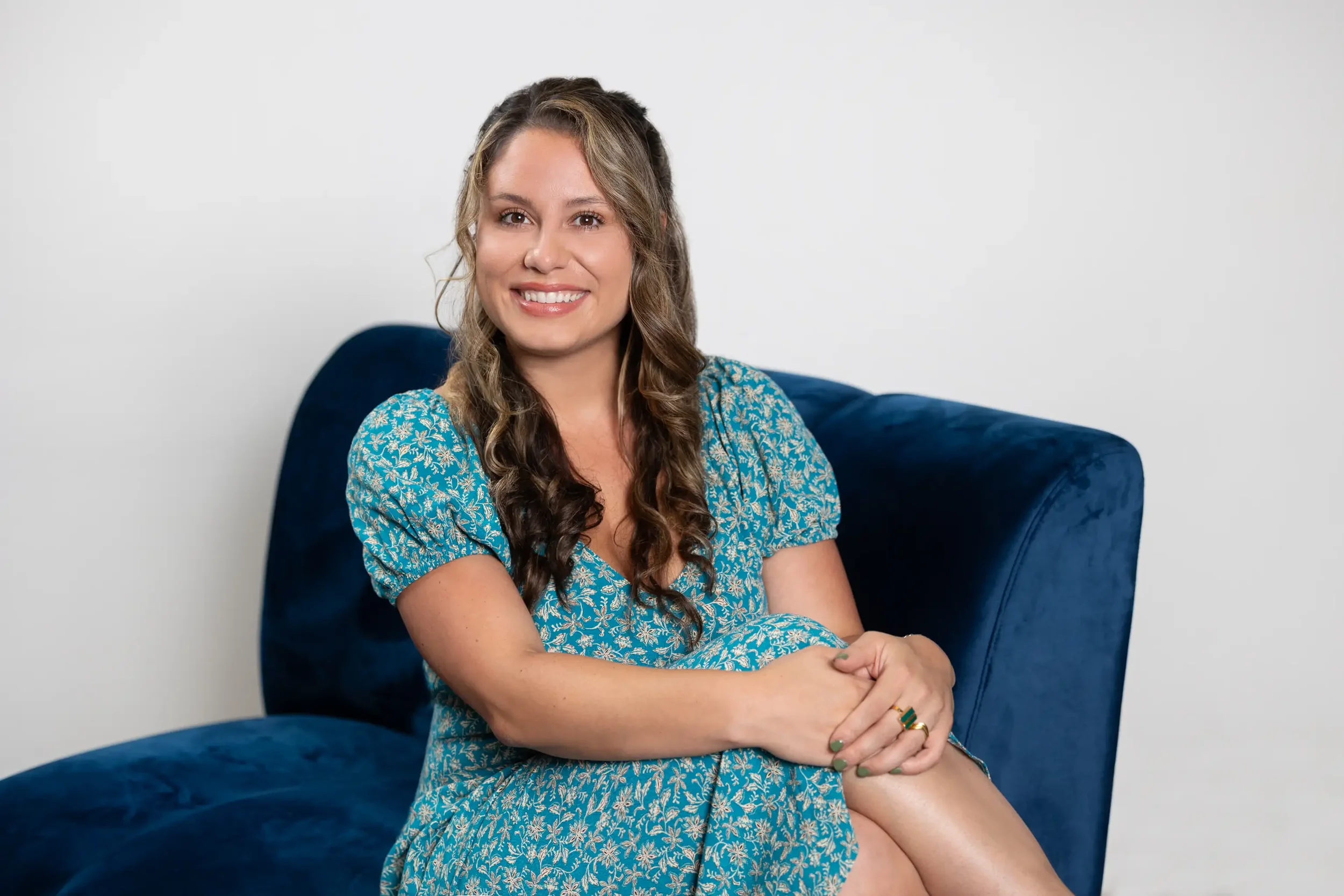 Grace Prete, pelvic floor therapist at The GSM Collective, seated on a navy velvet chair in a teal floral dress