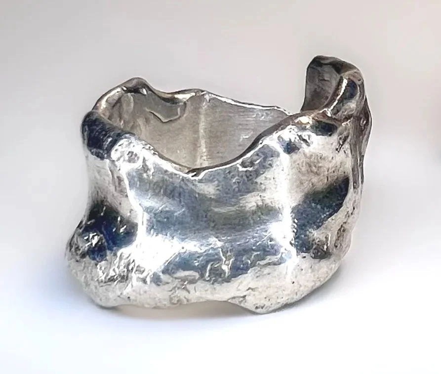 A silver, irregular-shaped metallic object that appears to be a piece of jewelry or art sculpture.