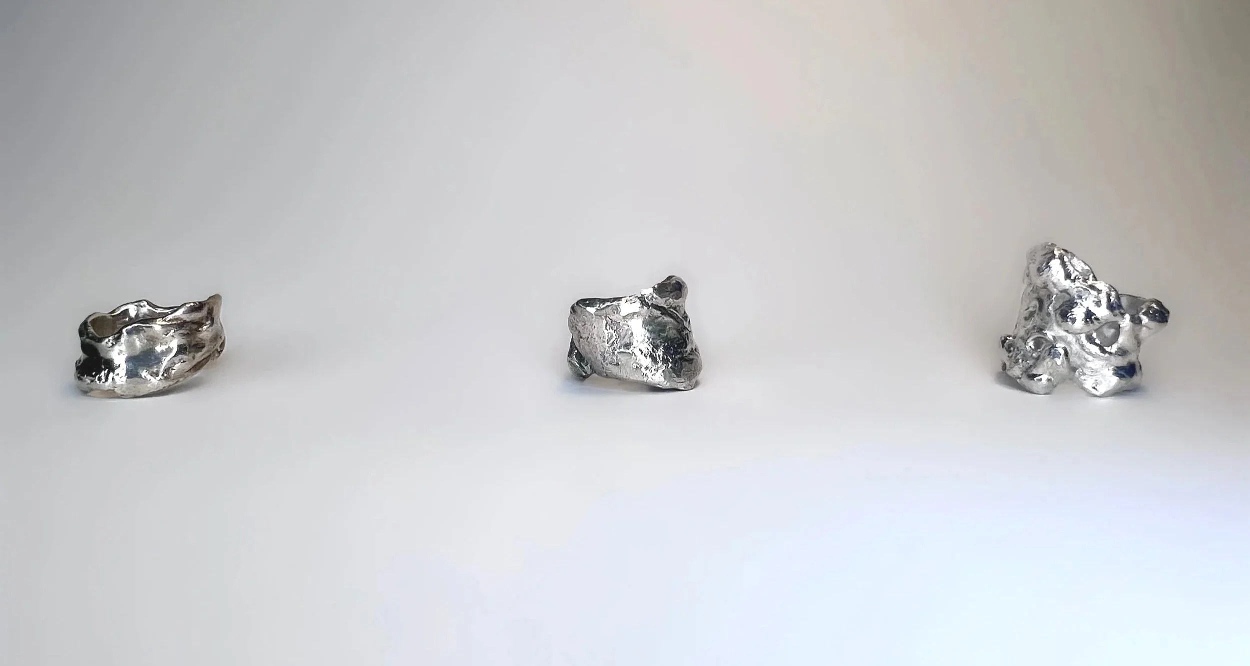 Three irregularly shaped silver rocks placed in a row on a plain white background.