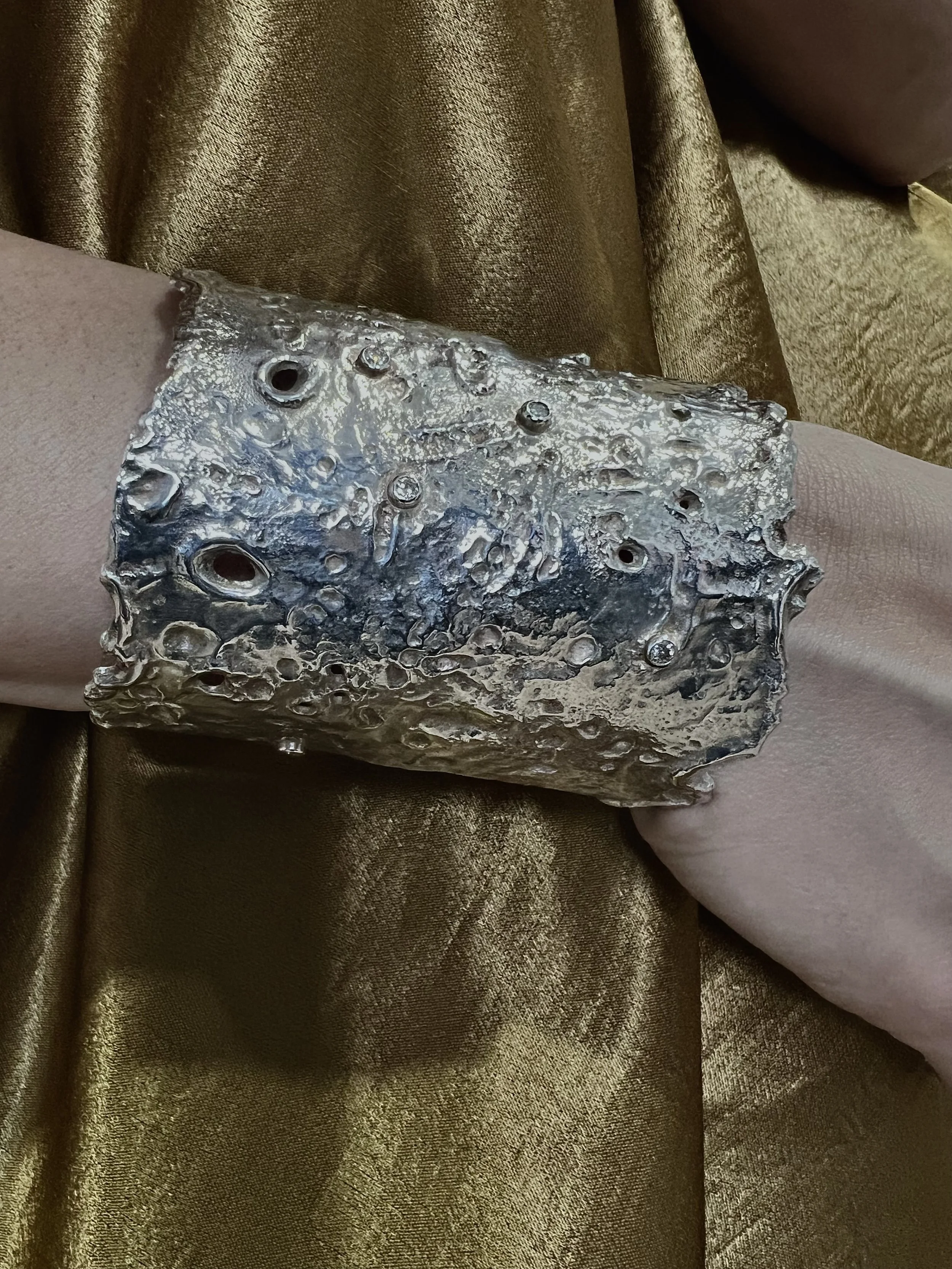 Close-up of a textured metallic object, possibly a piece of jewelry or decorative item, resting on shiny gold fabric.