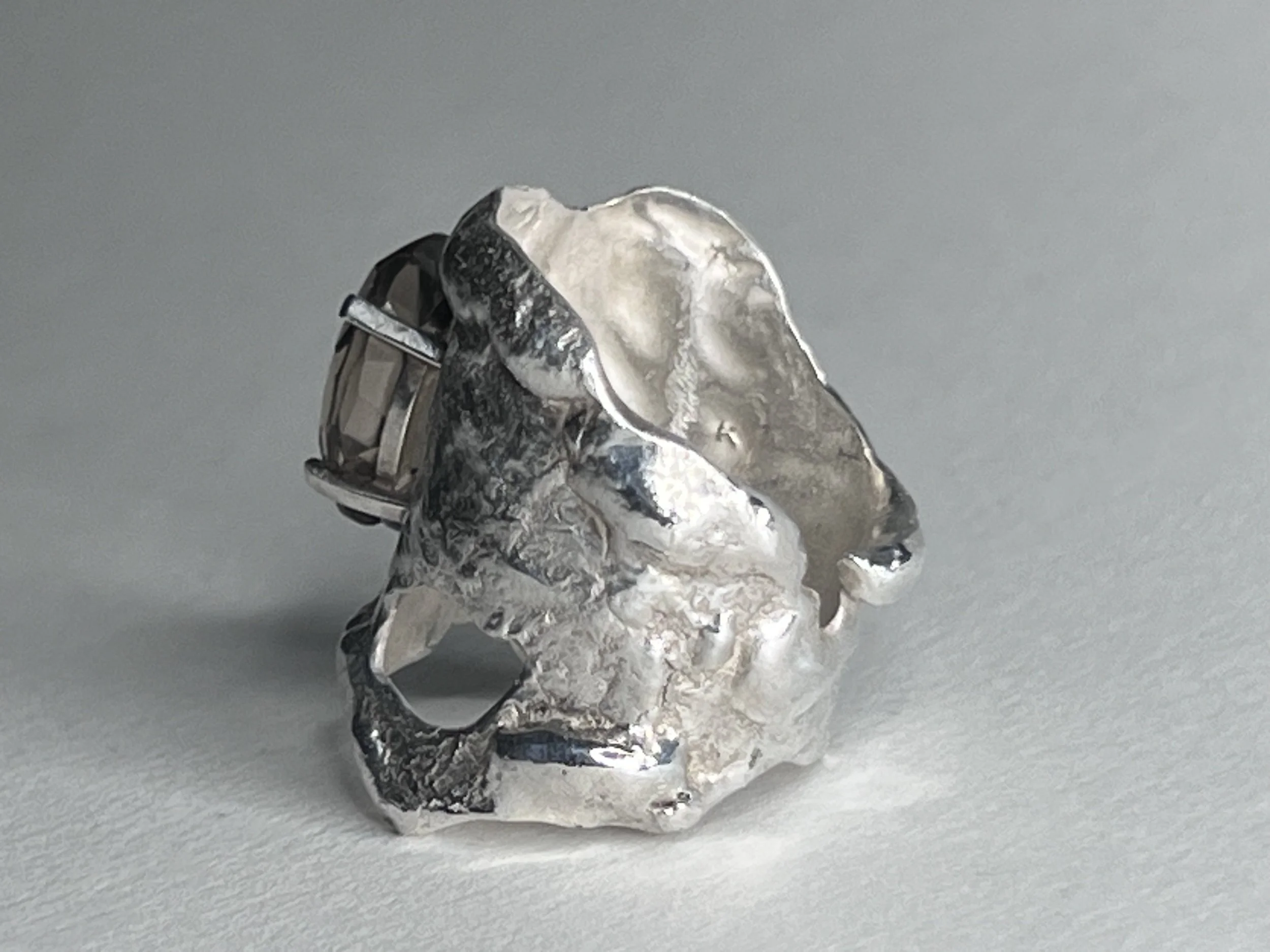 A small sculpture of a wizard in silver foil, wearing glasses and a pointed hat, with a large crystal ball in front of him, set against a plain light gray background.