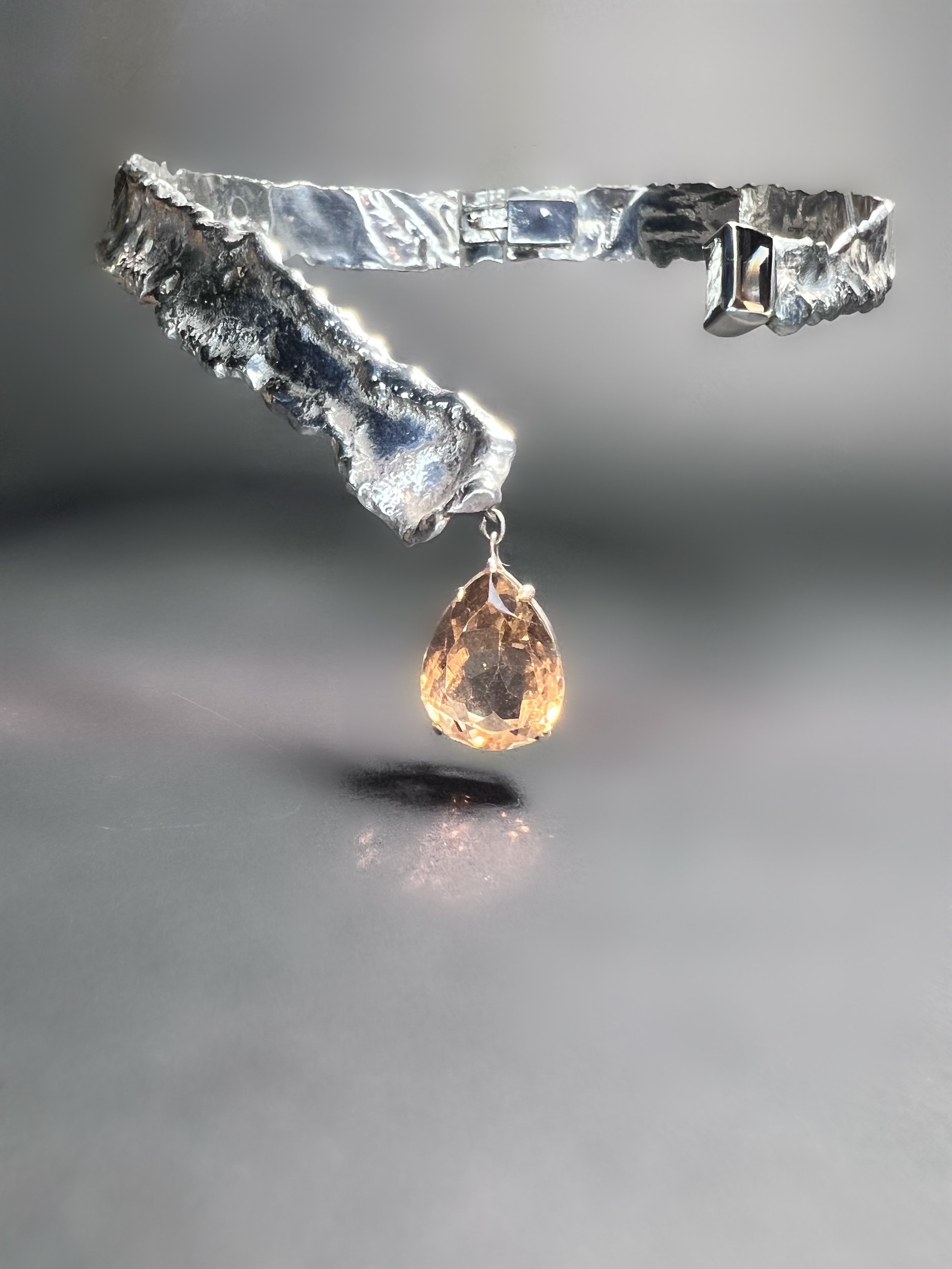 A jewelry piece featuring a rectangular gemstone and a teardrop-shaped gemstone, set in a textured silver band.