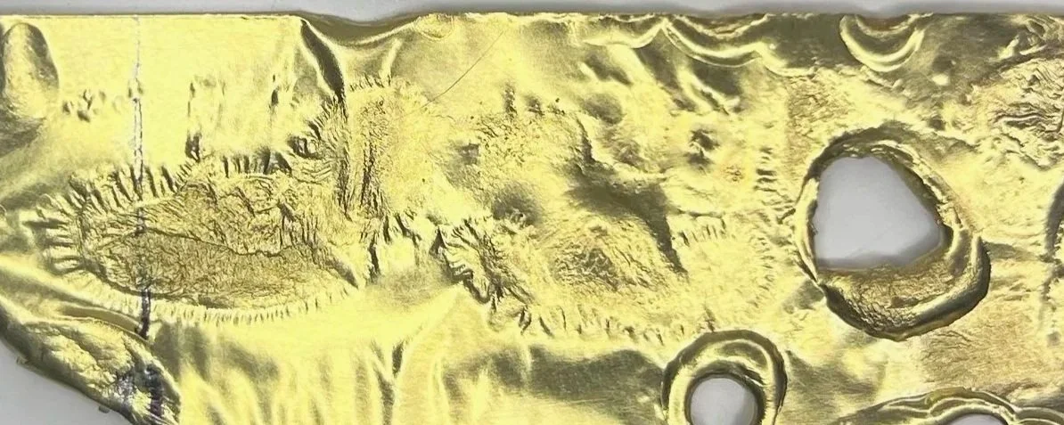 Close-up of a gold-colored metallic surface with embossed irregular patterns and circular indentations.