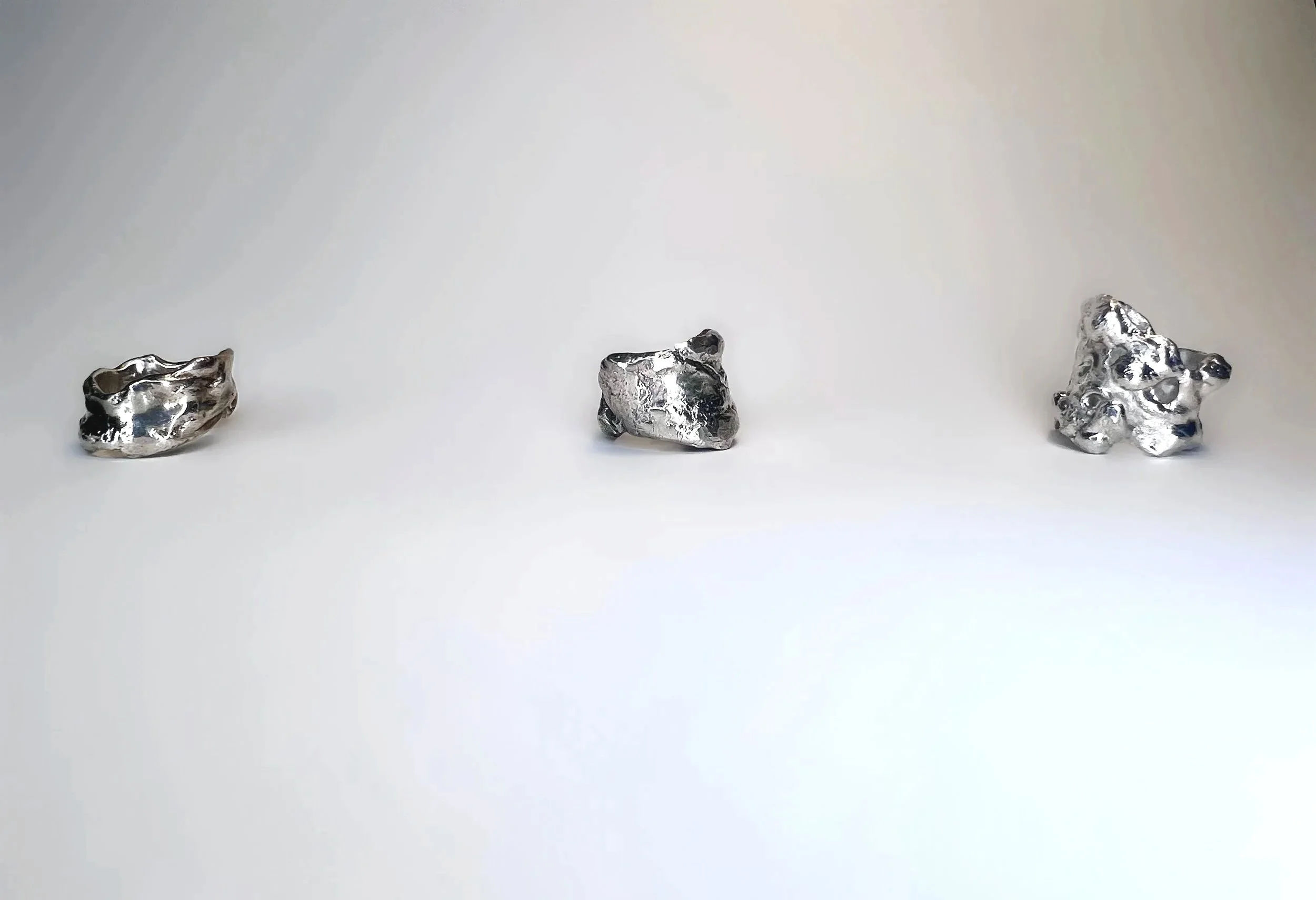 Three irregularly shaped metallic rocks or sculptures on a white background.