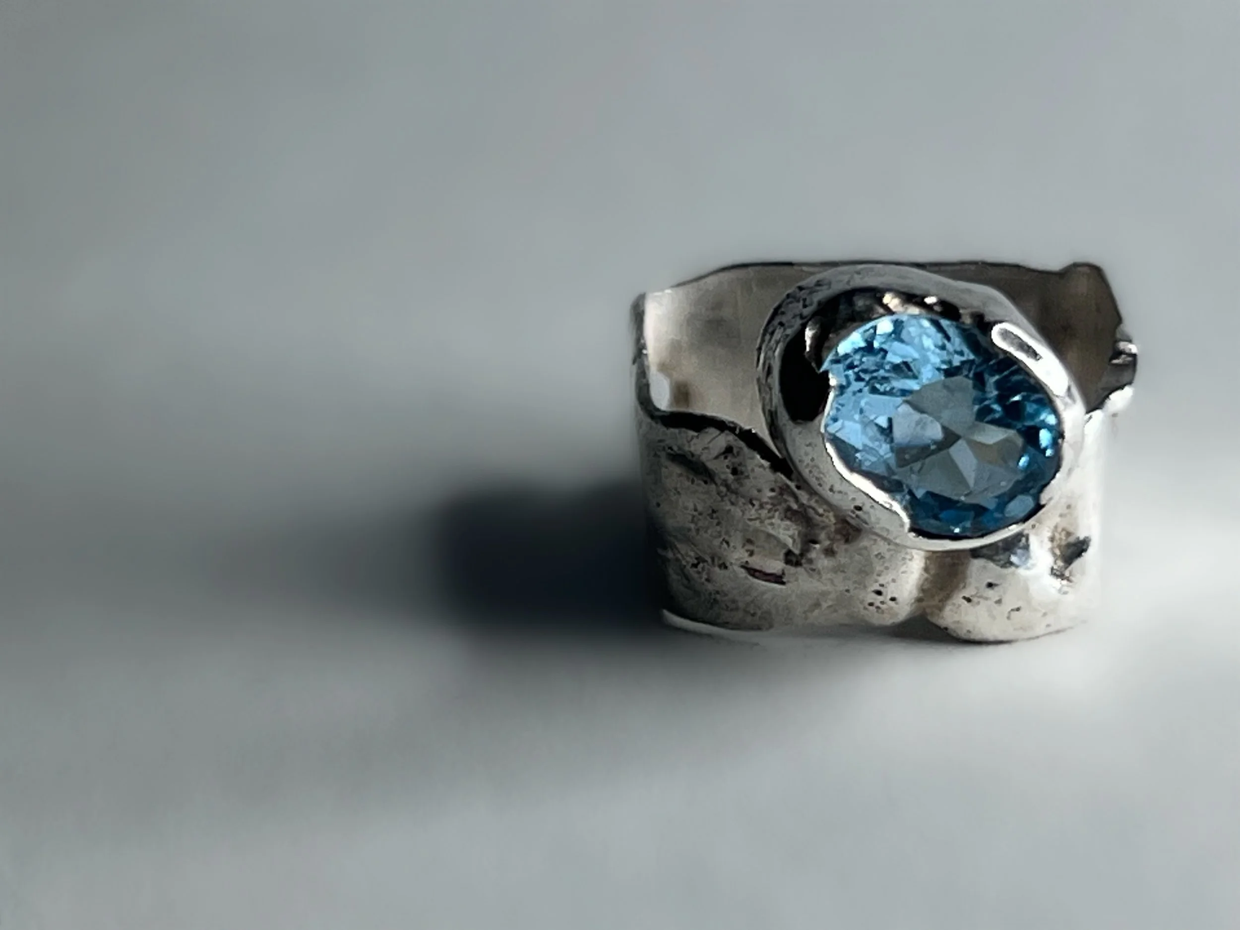 Close-up of a silver ring with a large, round-cut blue gemstone set in the center.